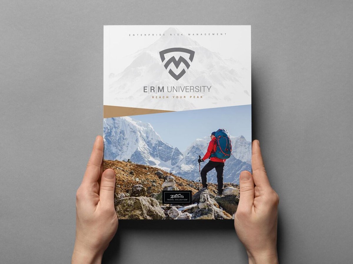 Hands holding a brochure titled 'ERM University' featuring a mountain climber on a rocky ridge with snow-covered peaks in the background.