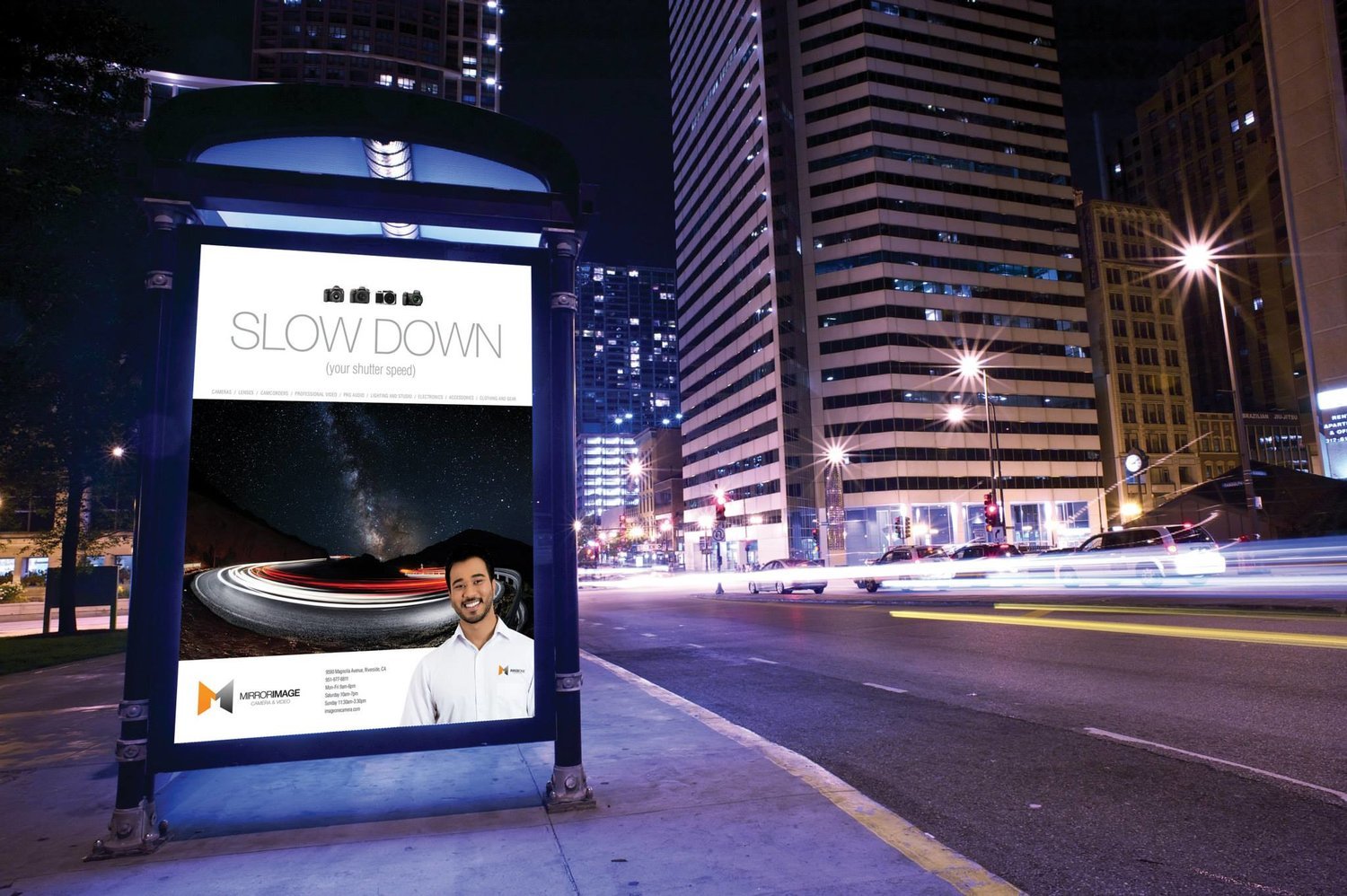 City street at night with a billboard ad for photography; text "SLOW DOWN (your shutter speed)"; background includes a night sky and light trails; skyscrapers and blurred car lights in the background.