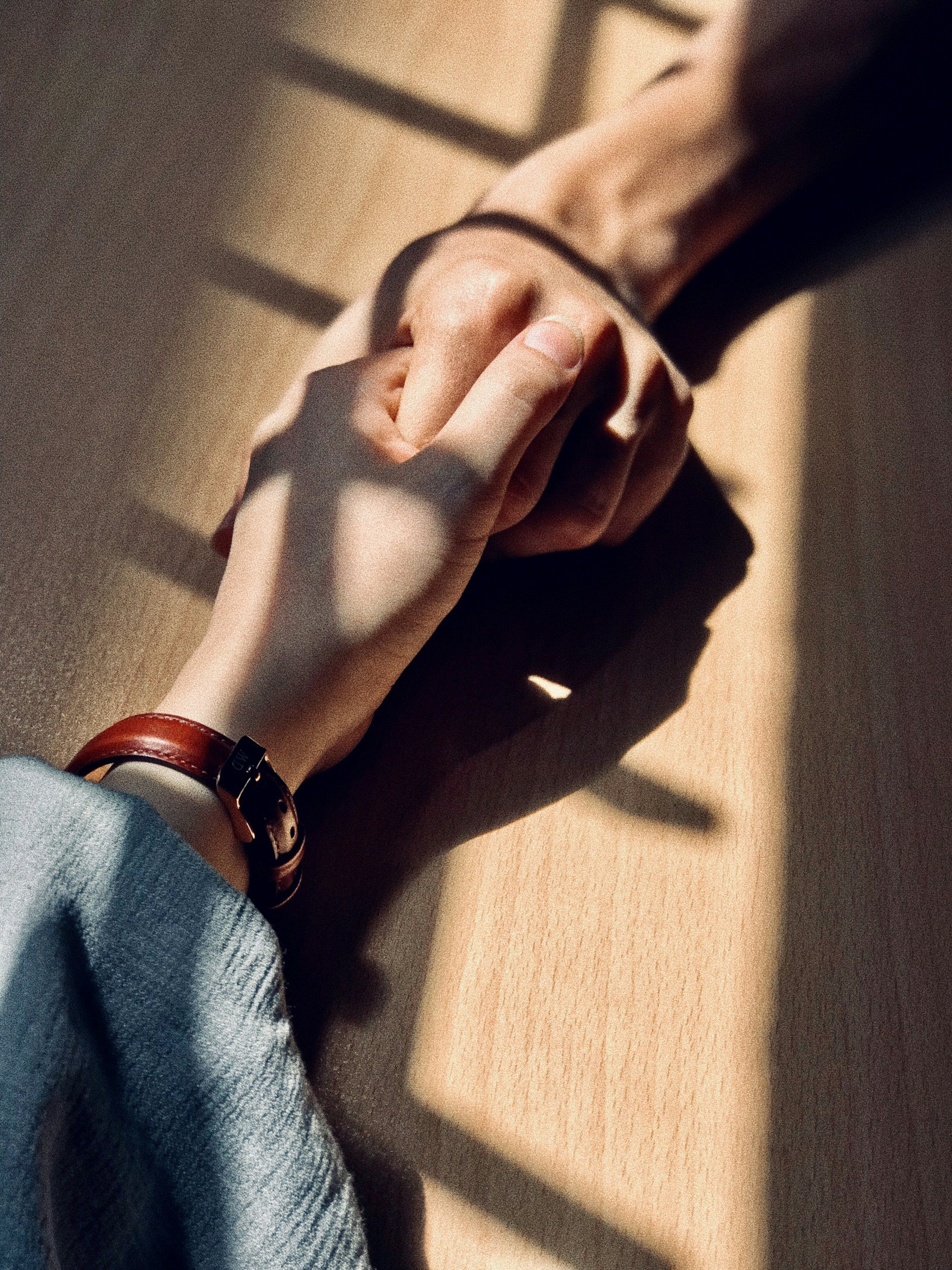 Close-up of two people holding hands on a wooden table, with shadows cast from a nearby window.
