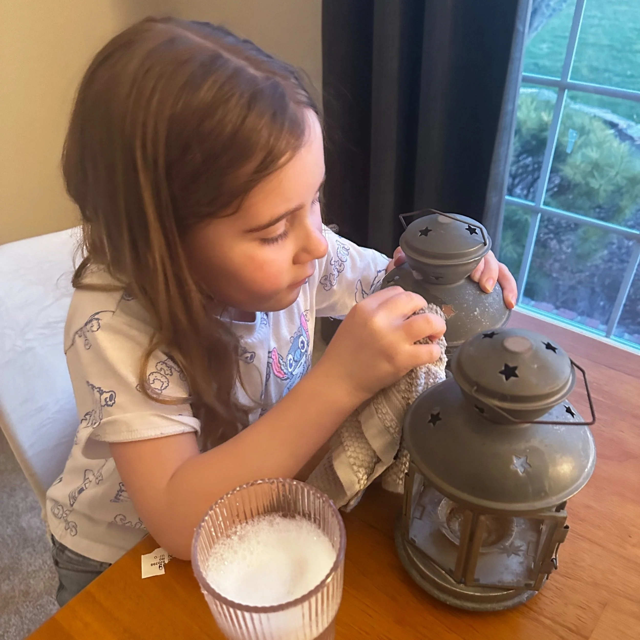 Little girl is carefully cleaning two lanterns with dish soap and warm water to repurpose them into colorful bird houses.