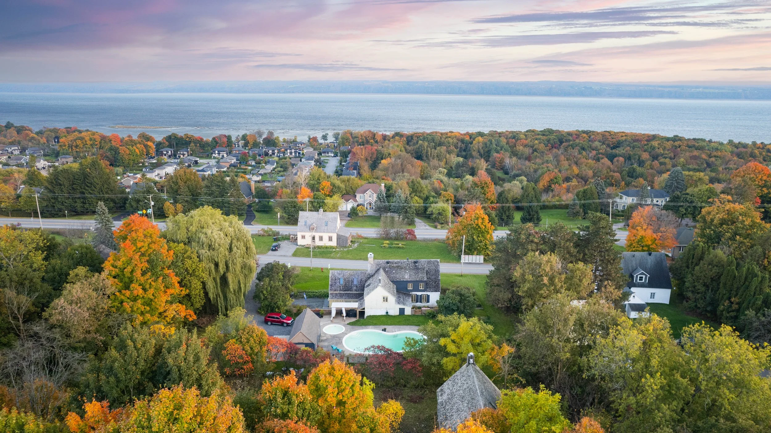 Vue aérienne de maisons résidentielles au printemps avec arbres colorés et un lac en arrière-plan.