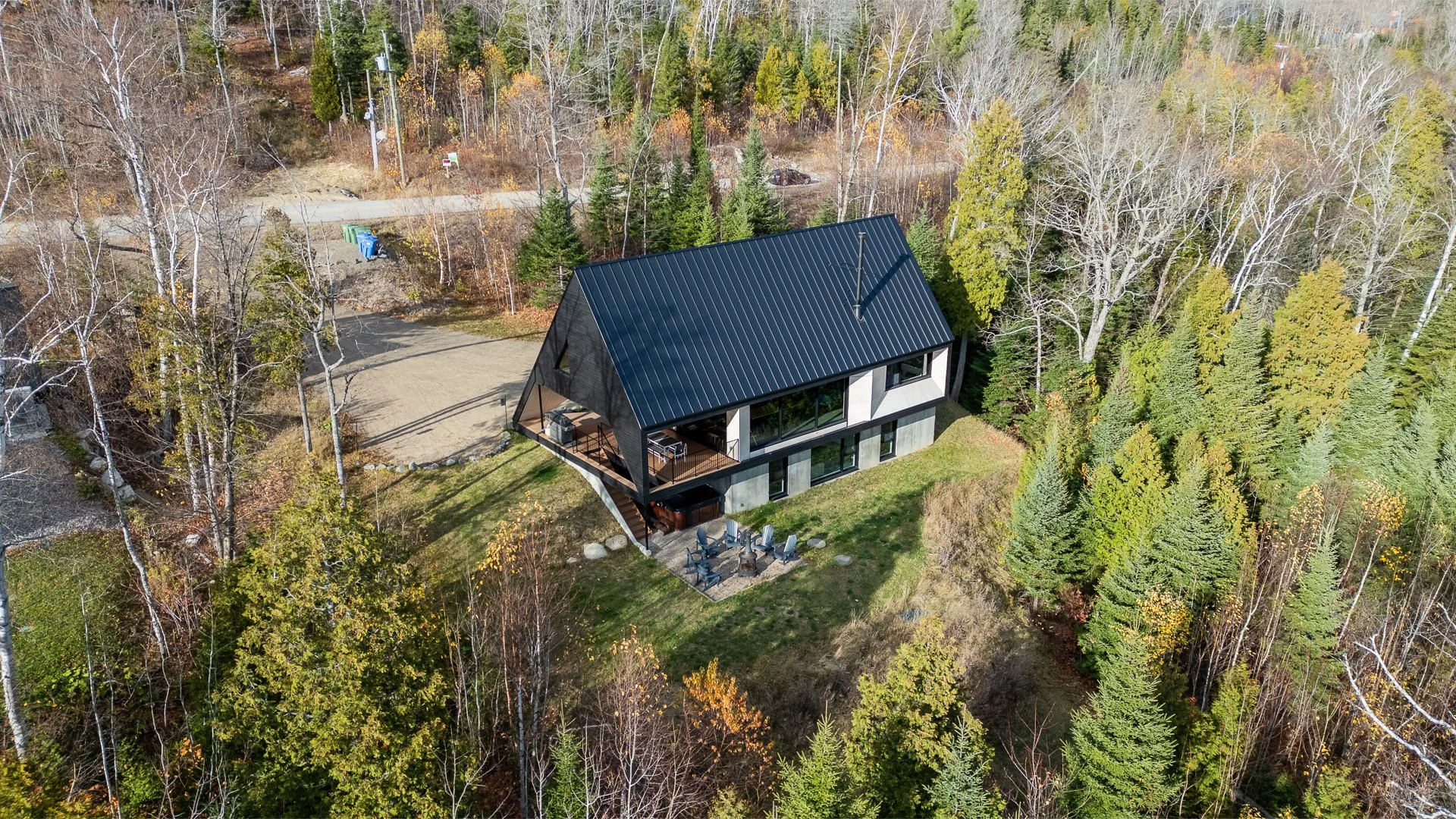 Une maison moderne avec un toit en métal noir, entourée d'arbres en forêt pendant l'automne, vue aérienne.