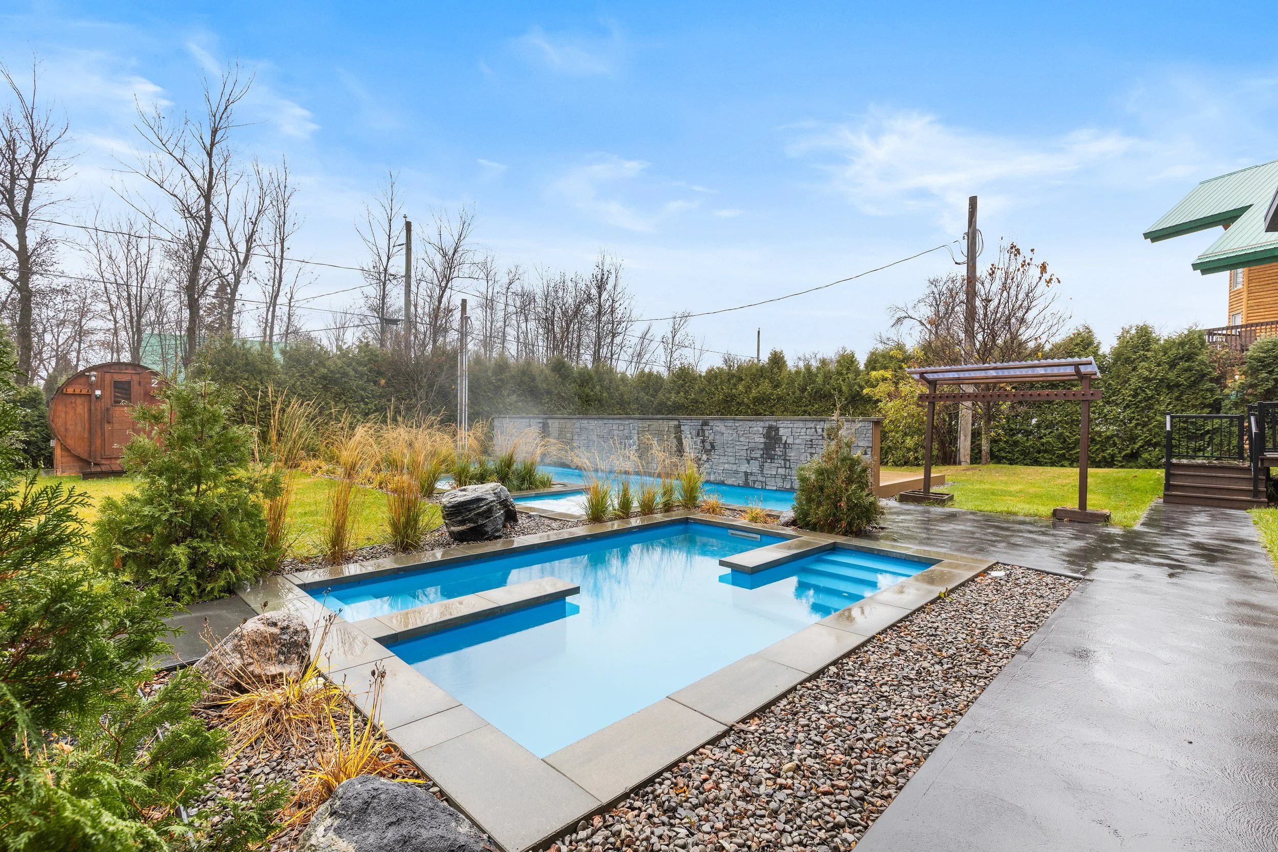 Piscine moderne avec spa dans un jardin paysager, arbres nus et ciel bleu