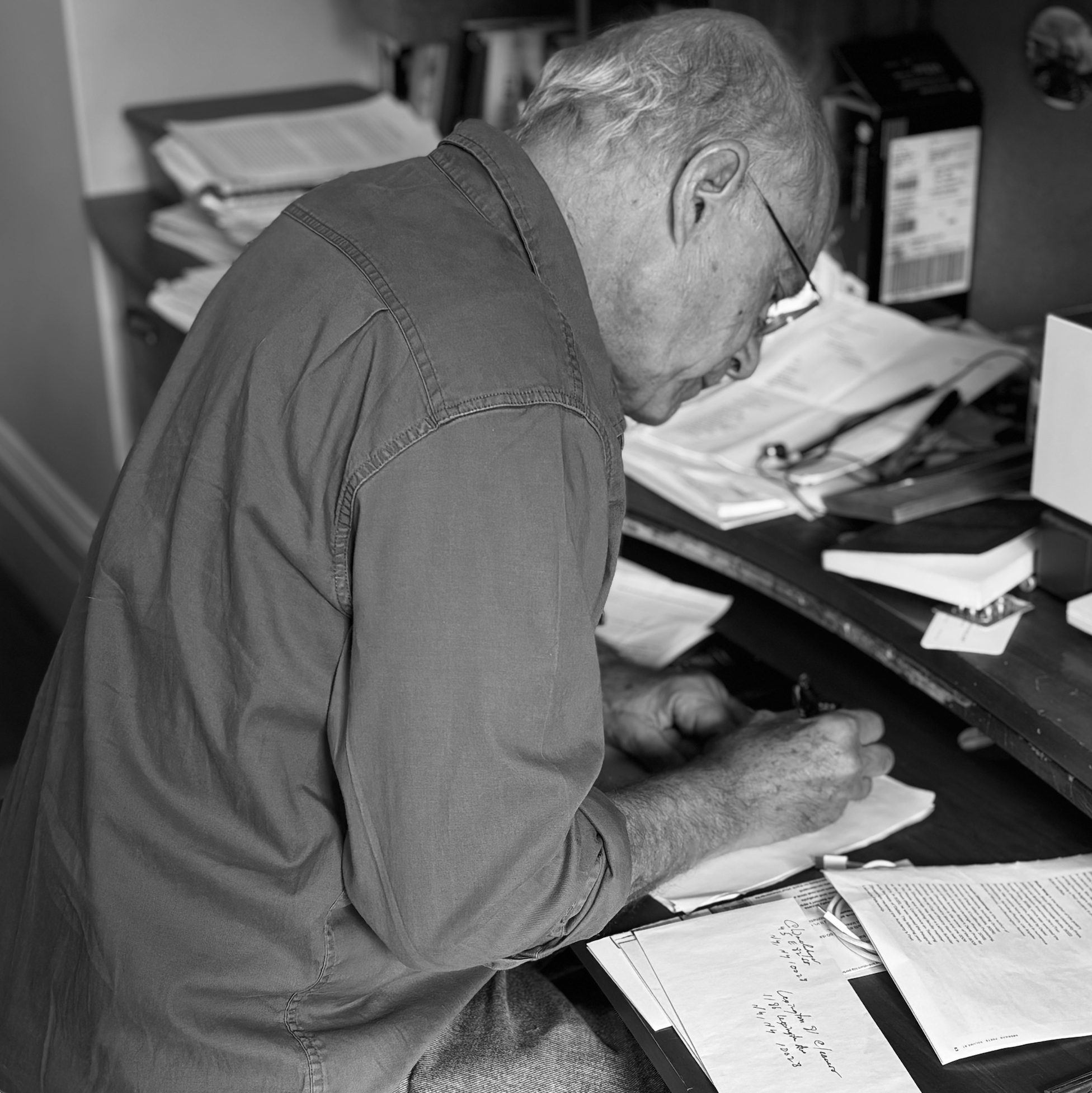 A black and white photo of Chaim Wachsberger, a older white man with glasses writing at a desk