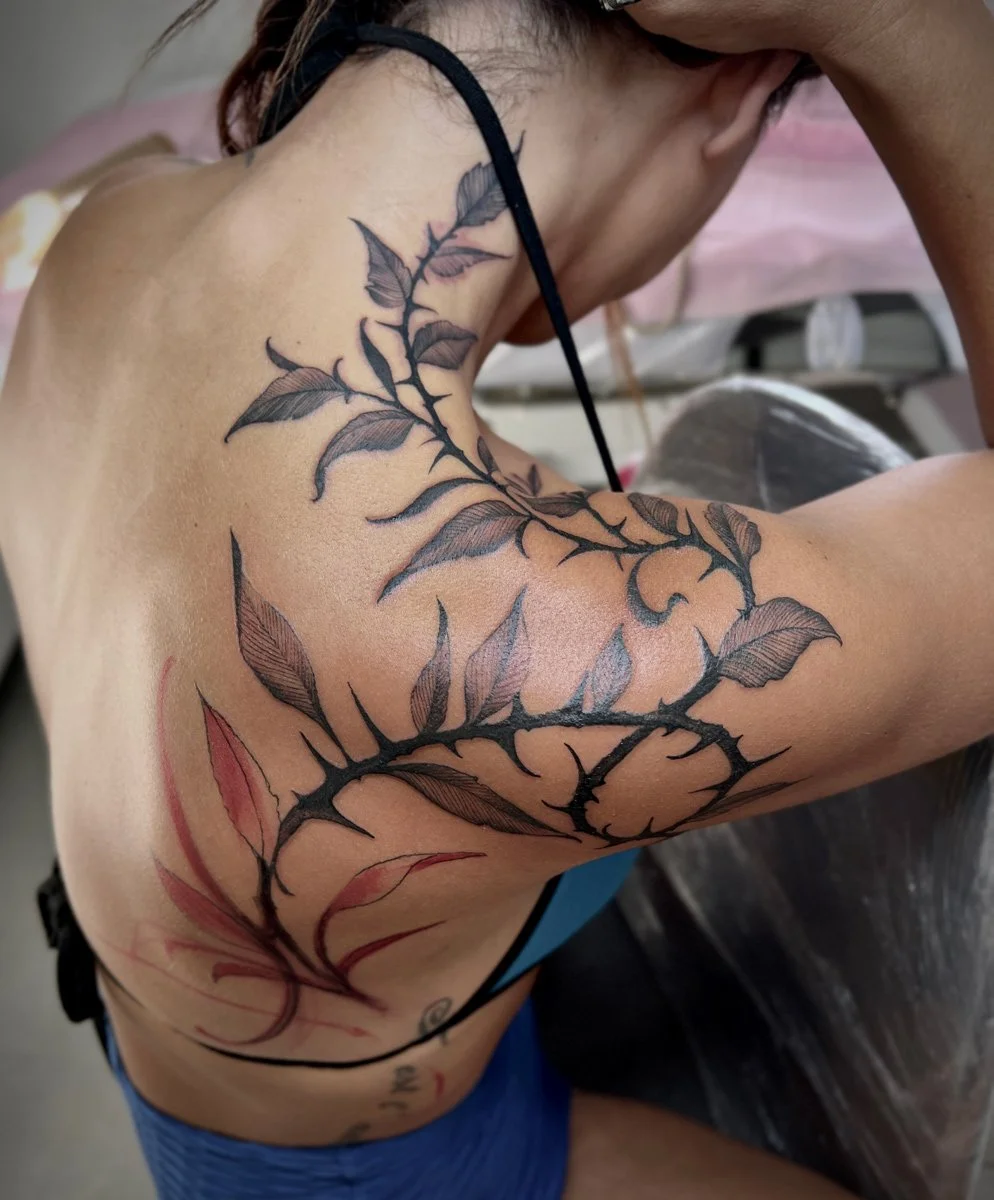 A person with tattooed florals on their shoulder and upper arm, featuring black and red ink, in a tattoo studio.