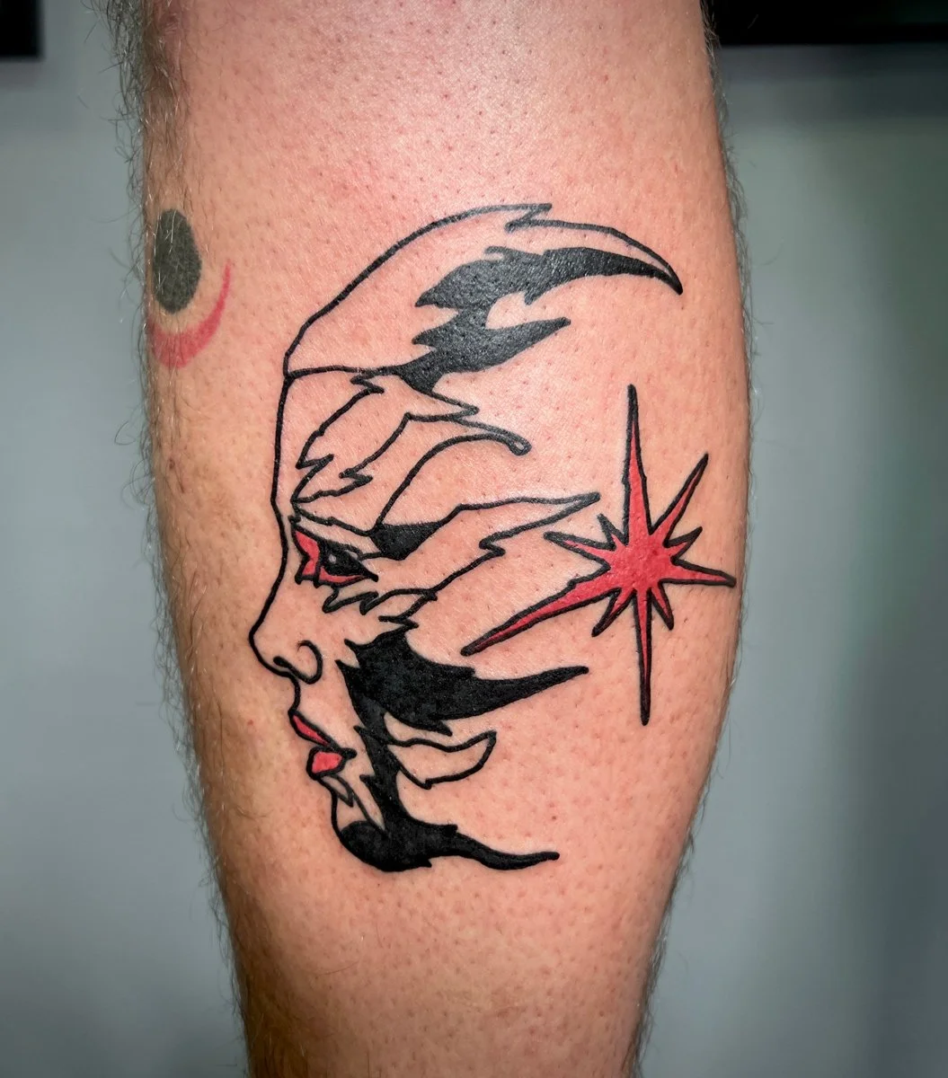 Tattoo of a woman's face in profile with closed eyes and red lips, combined with abstract black shapes and a red starburst on the cheek.