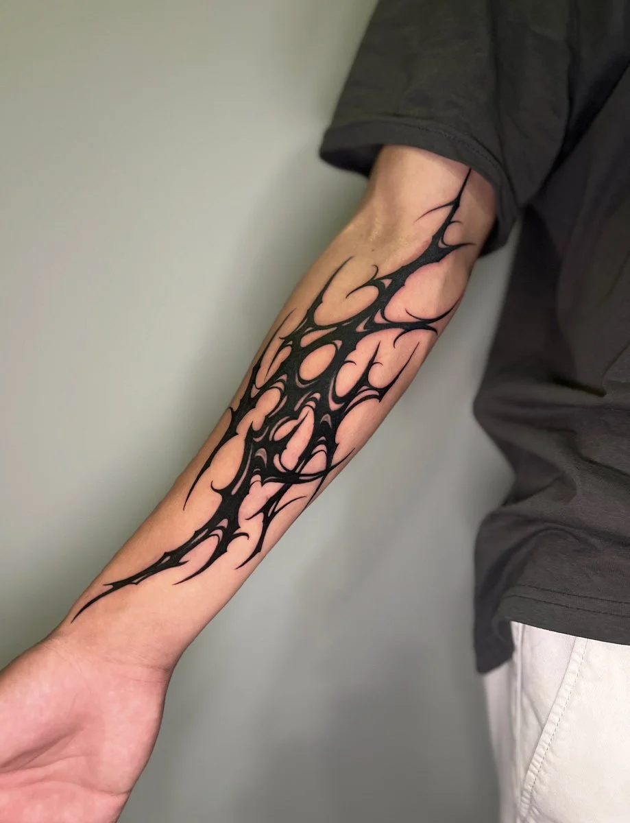 A person's arm with a black tribal-style tattoo, extending from the wrist to above the elbow, against a plain background.