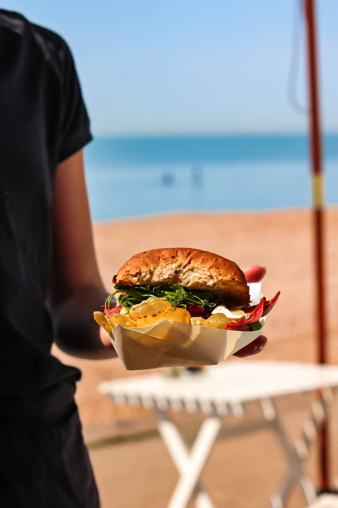 Person holding a sandwich with a beach and ocean in the background.