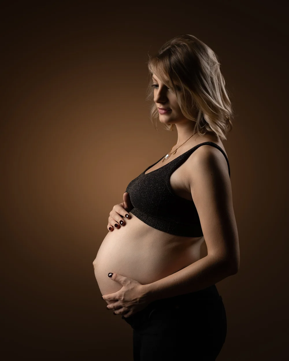 Femme enceinte de profil sur fond brun, séance photo grossesse en couleur à Rouen
