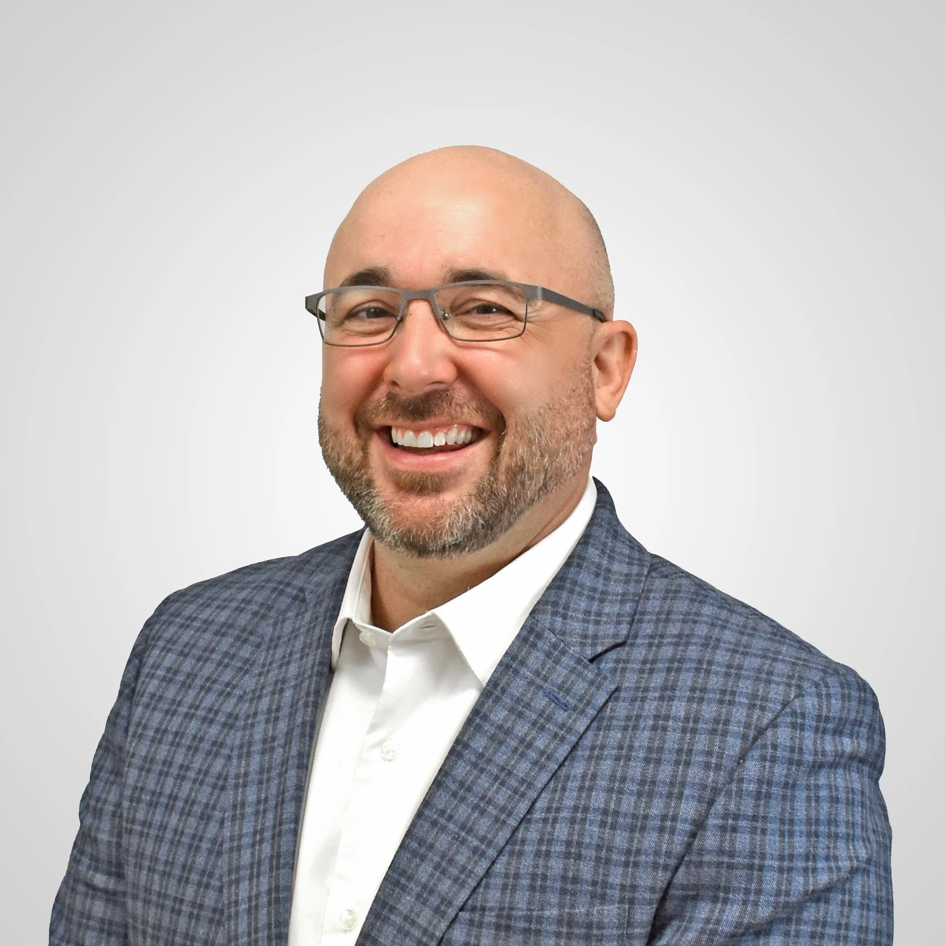 A smiling man with glasses, a beard, and a shaved head, wearing a blue shirt, against a white background.