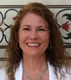 A woman with curly hair smiling in front of a decorative wall with floral patterns.