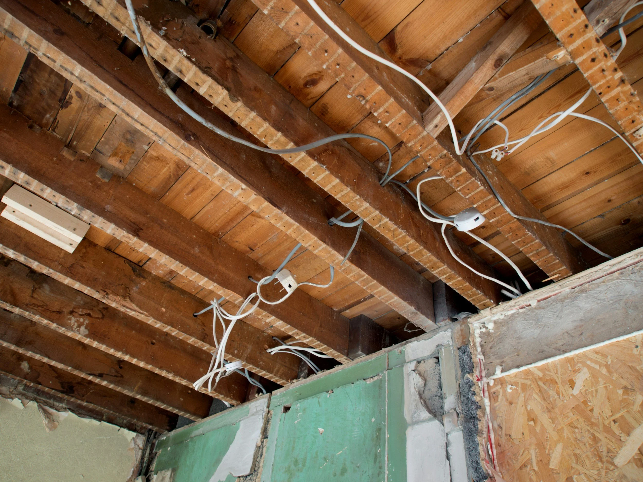 Wiring installed on a wooden ceiling of a building under renovation, with exposed beams and electrical cables hanging.