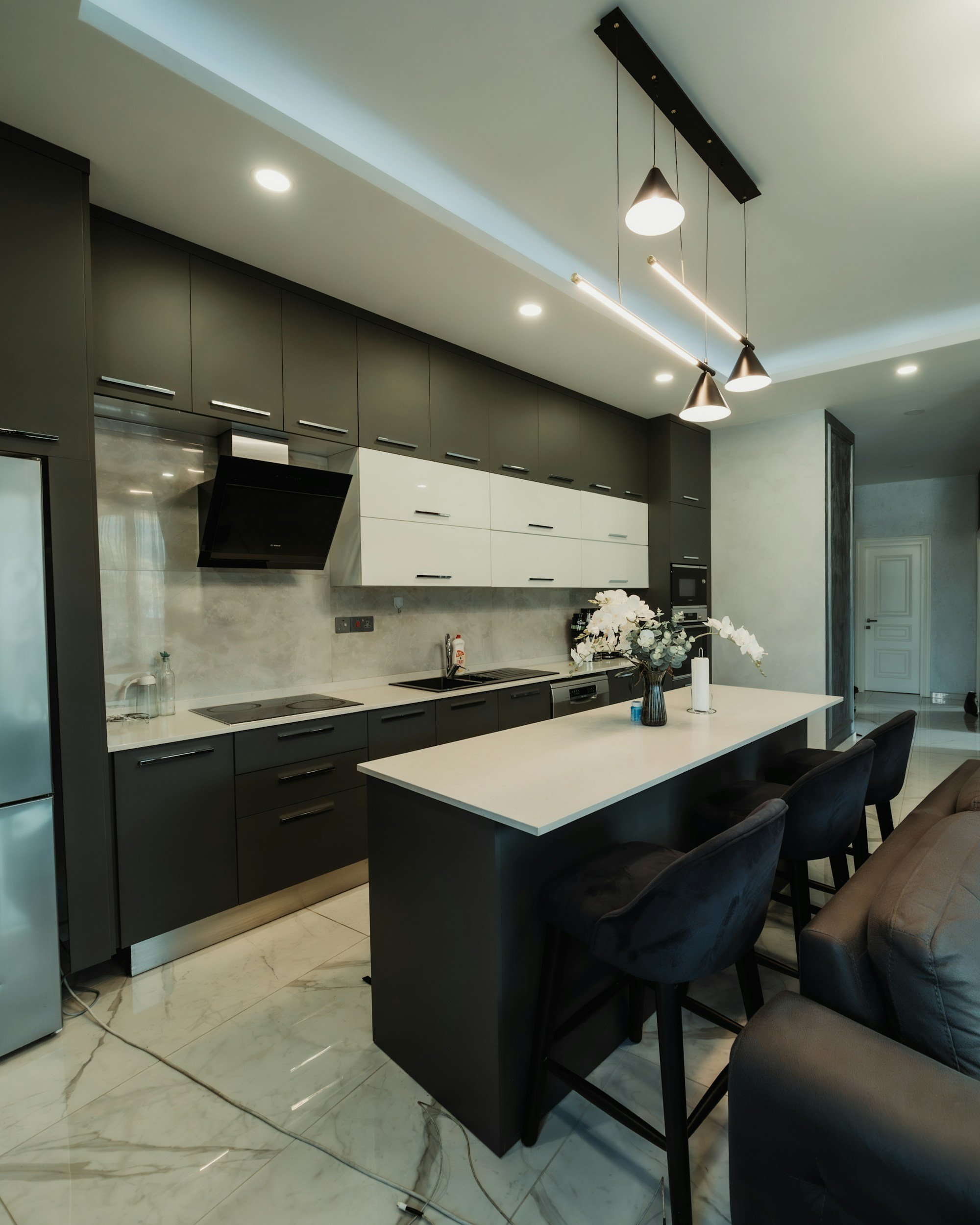 Modern black and white kitchen with an island, floral centerpiece, and hanging pendant lights.