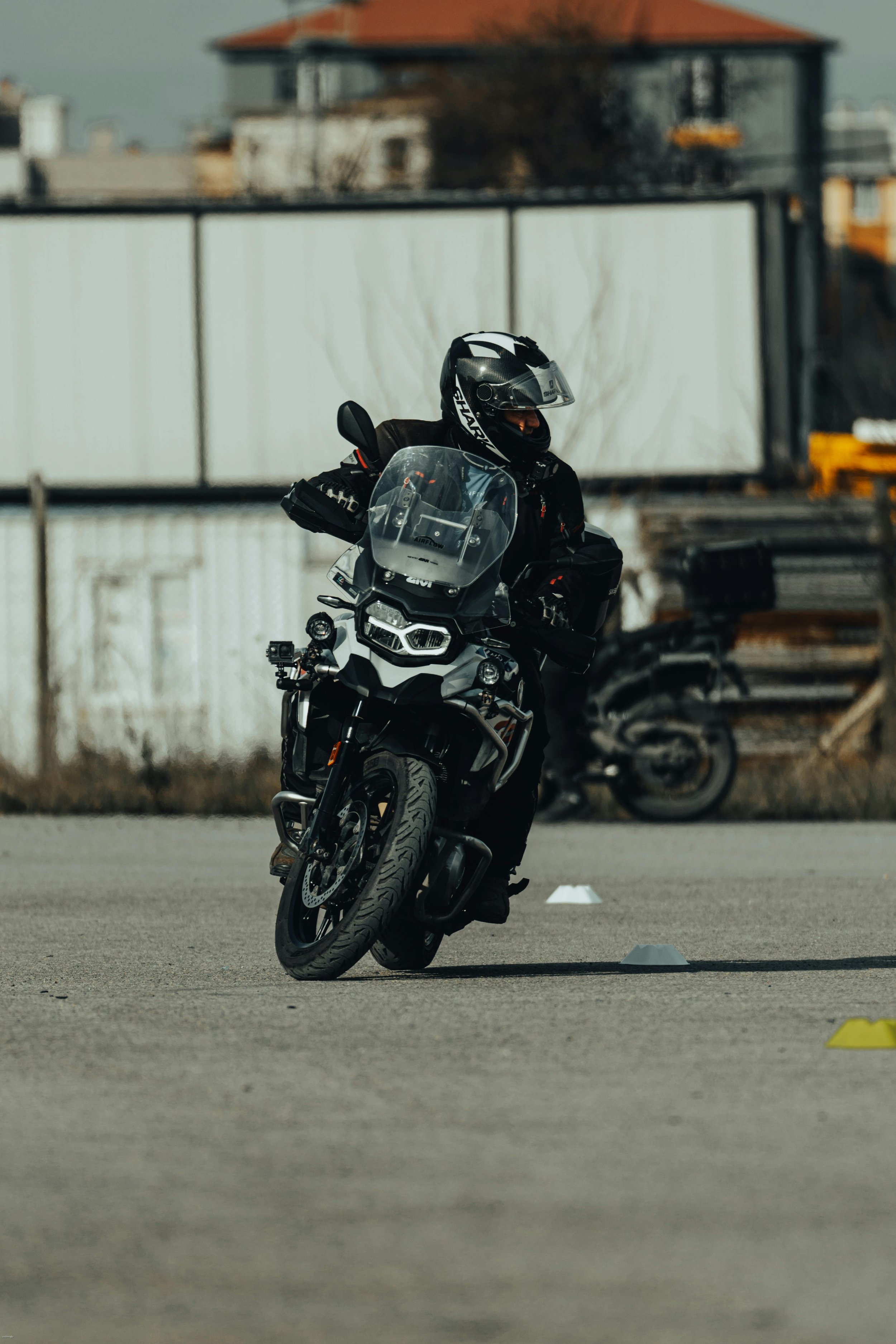 A motorcyclist in black riding gear and a helmet riding a black adventure motorcycle through an obstacle course set up with small cones outdoors.
