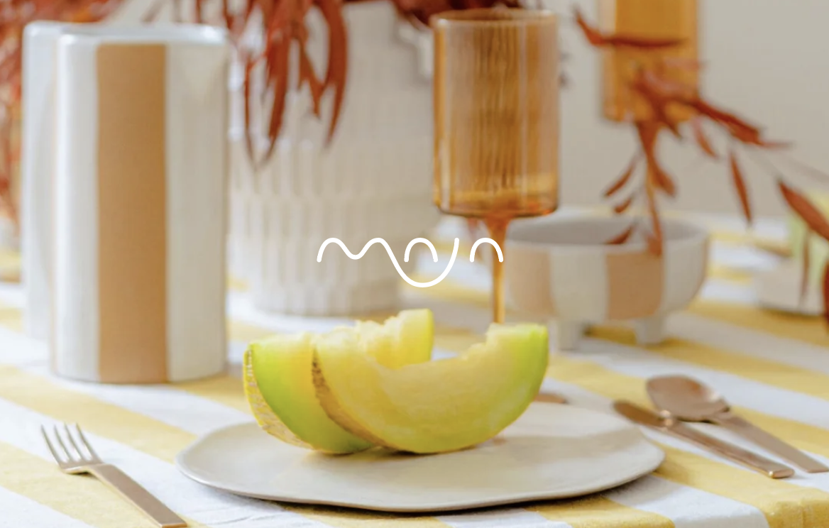 Maja Interior Designer's logo displated over a tablescape she designed, featuring a white logo over an image containing canteloupe on a plate.