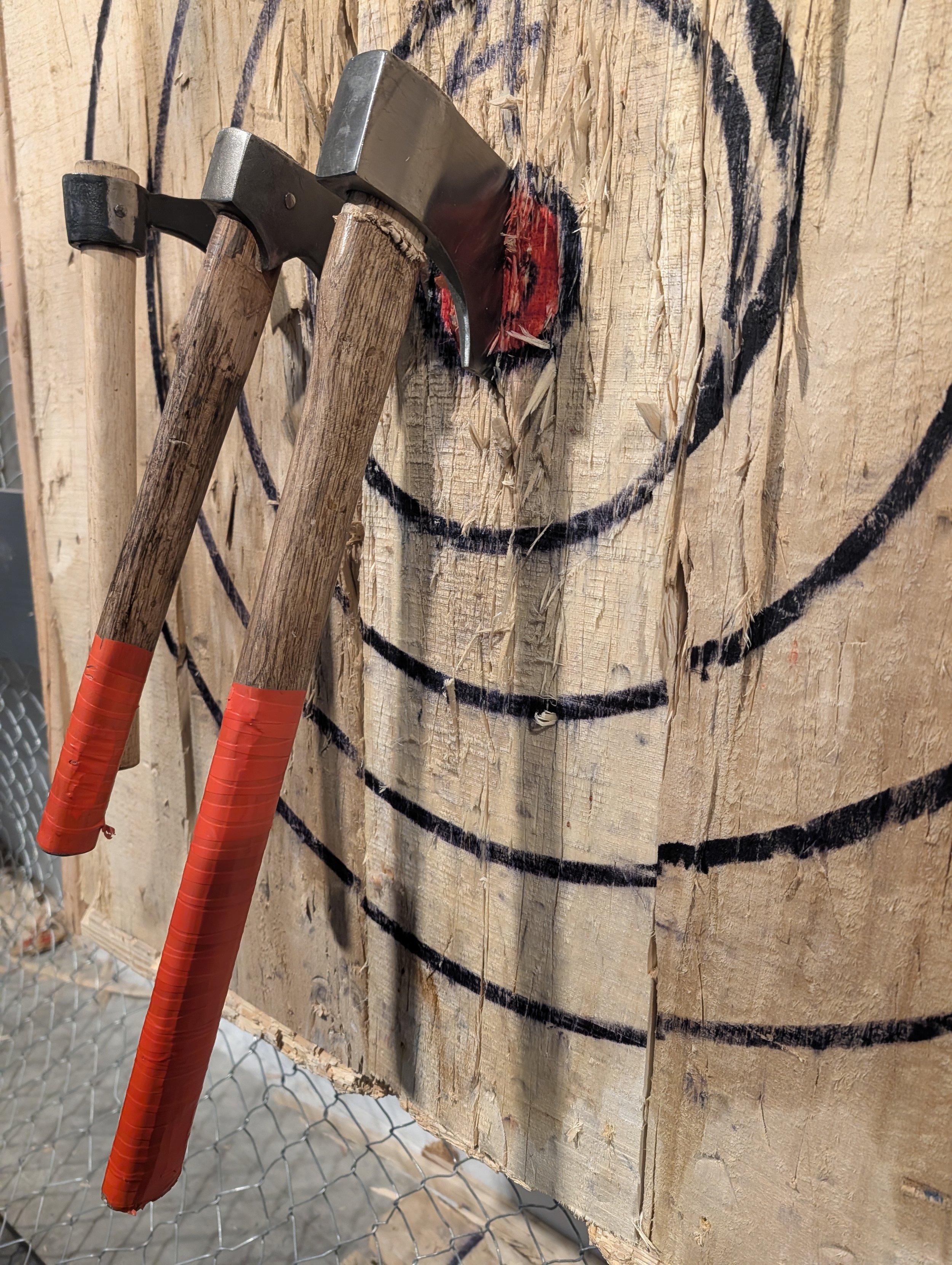 Three axes lined up on a wooden axe throwing board with the nearest in the bullseye