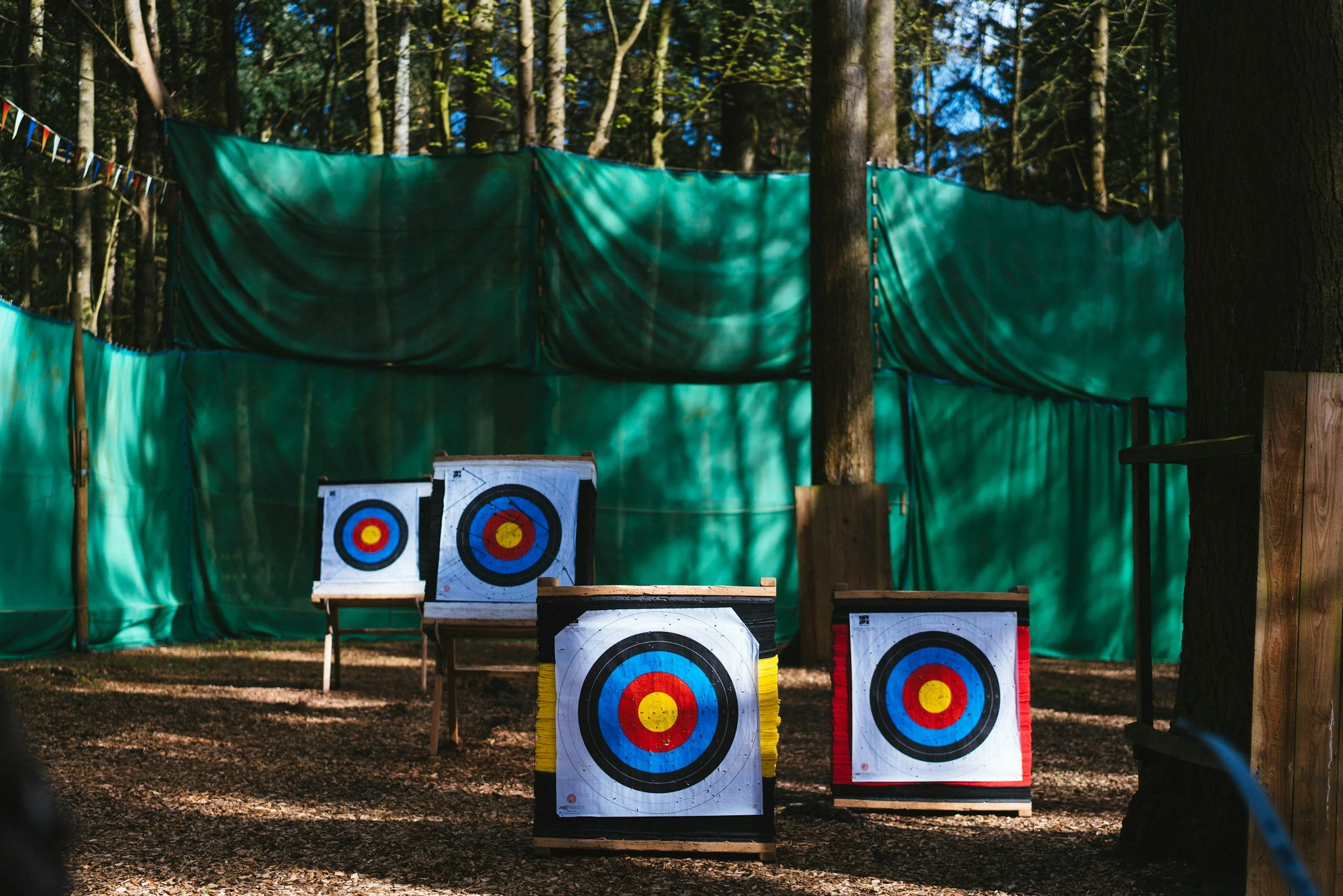An example of archery targets lined up at different distances from the archer. There is a green tarp in the background, along with trees.