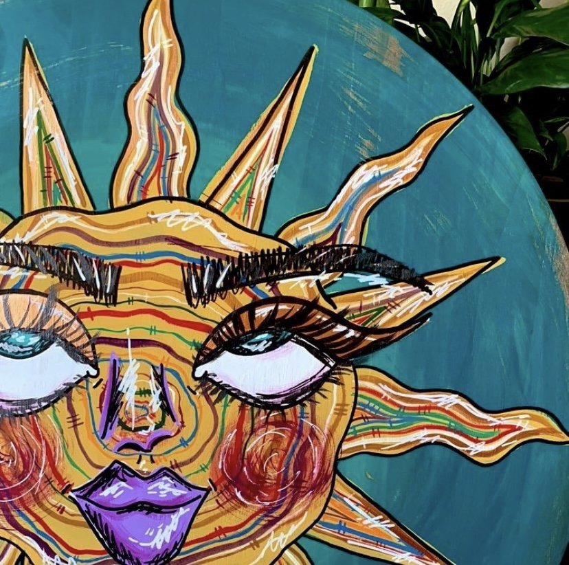 Colorful abstract painting of a sun with a face, featuring prominent eyes and purple lips, against a blue background.