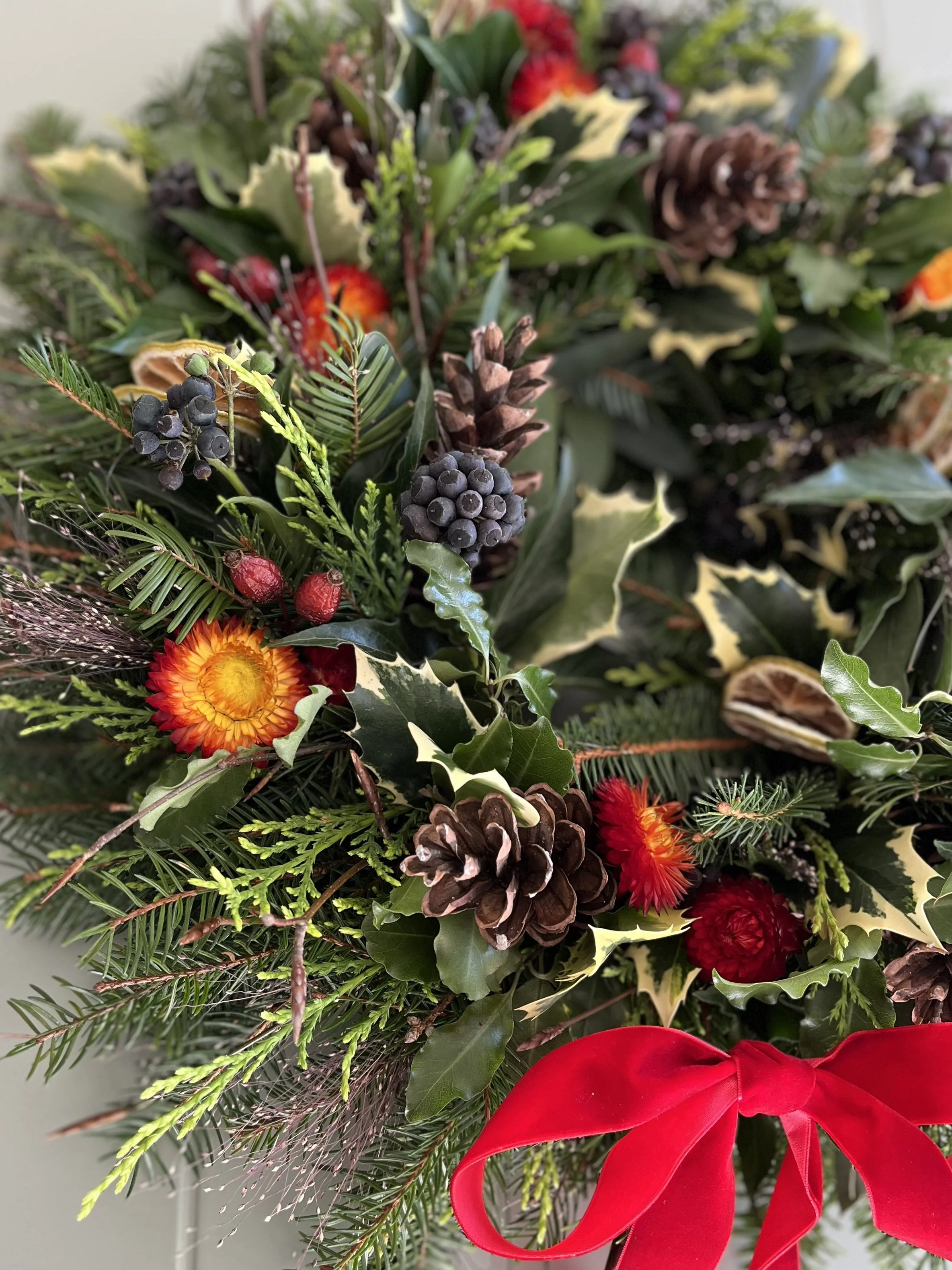 Handmade festive Christmas wreath featuring fresh greenery, pinecones, and a vibrant red ribbon by Little Leaf Floral in Berkshire