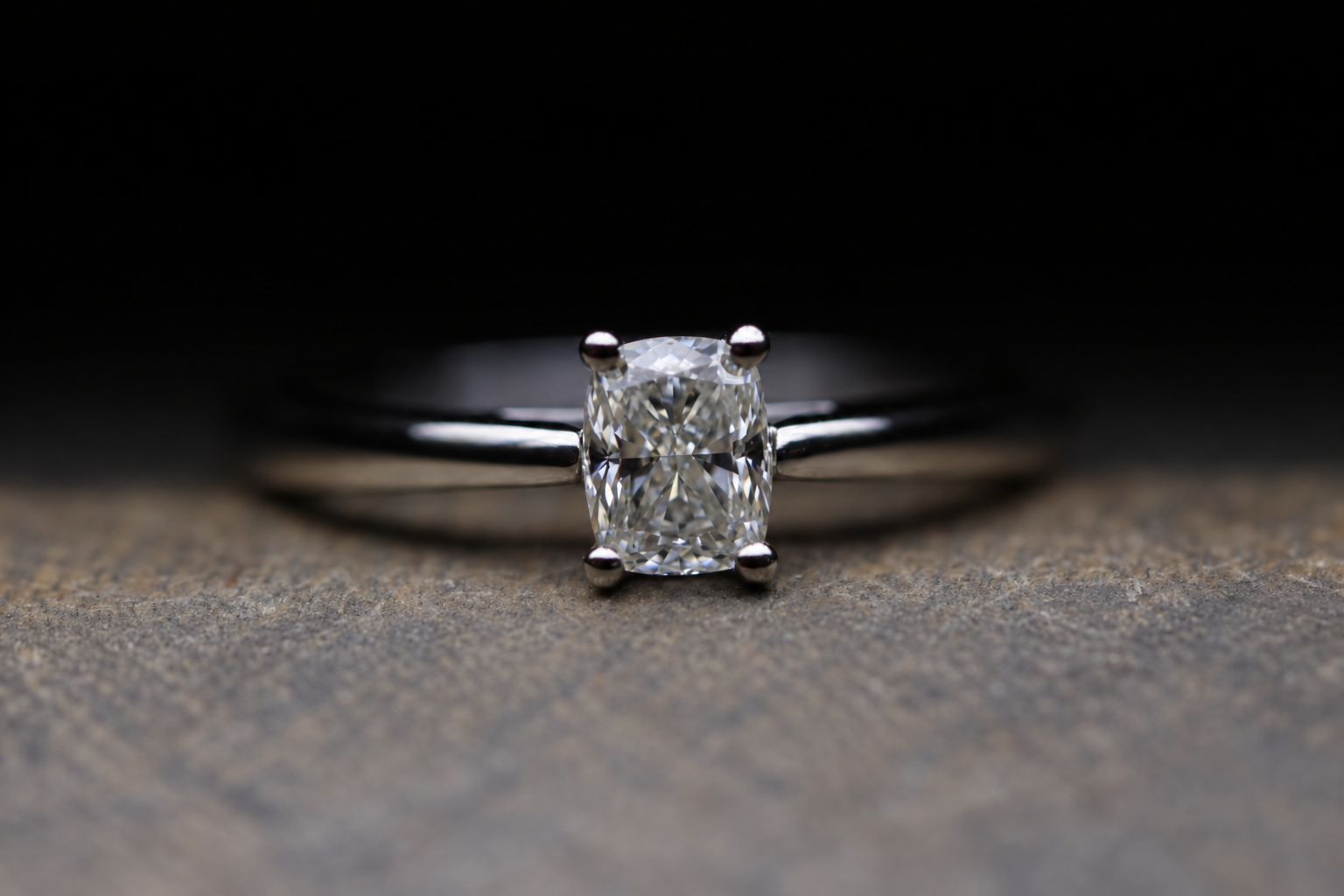 Close-up of a silver ring with a large cushion-cut diamond on a textured surface.