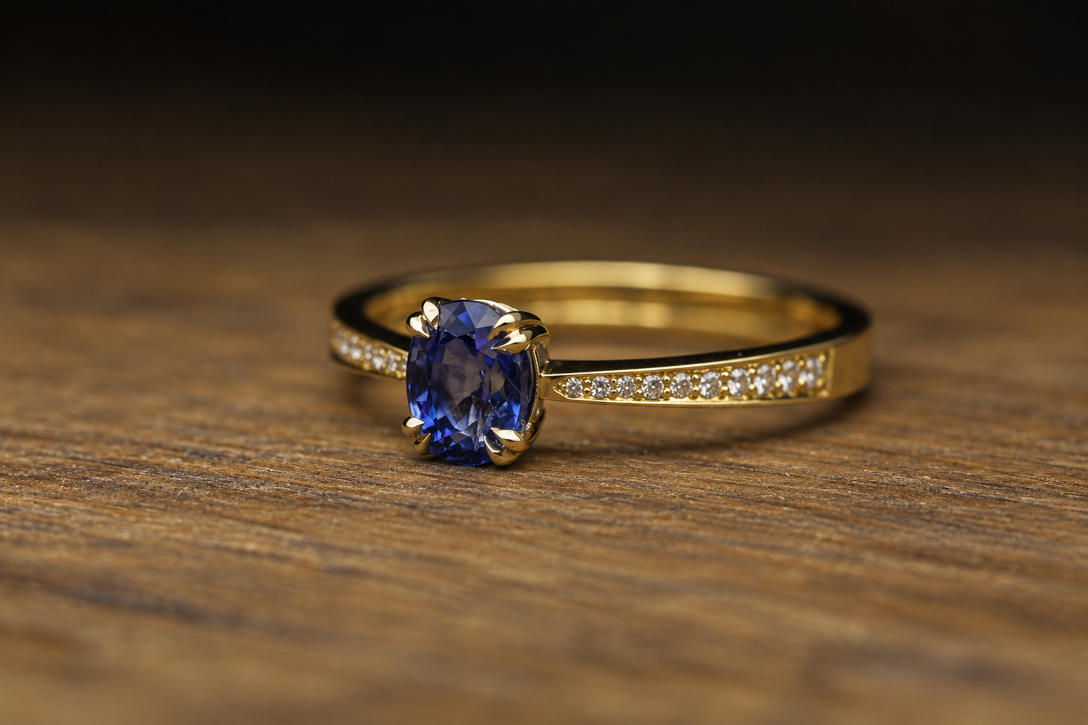 A gold ring with a large oval deep blue gemstone and small diamonds on the band, resting on a wooden surface.