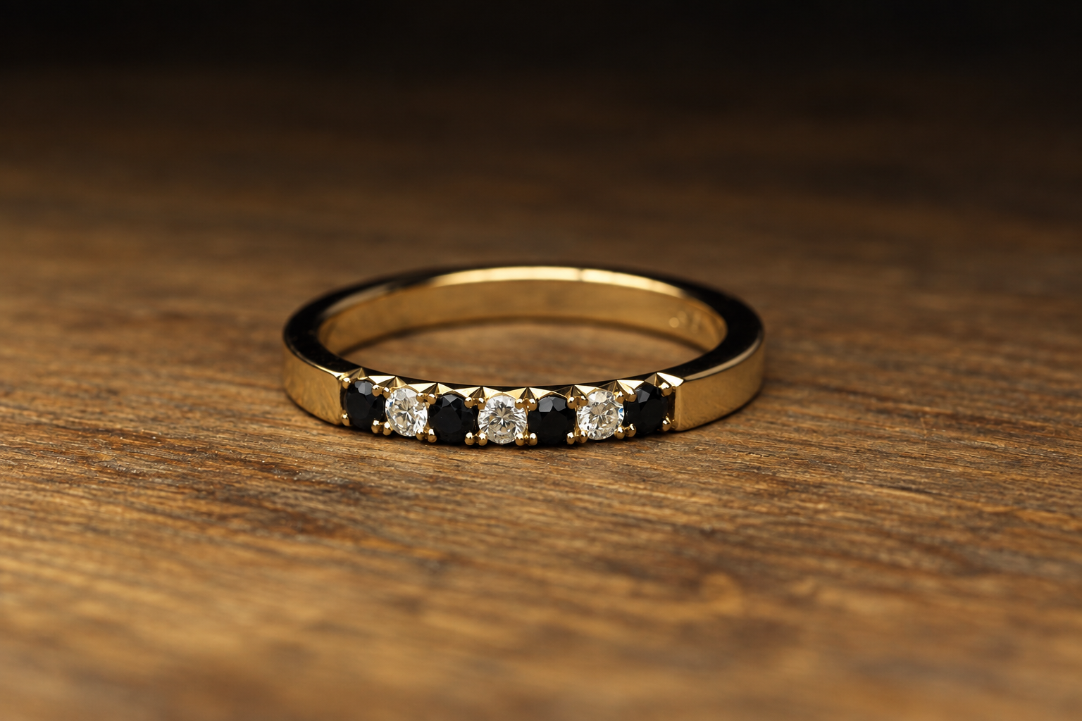 Gold ring with alternating black and white gemstones on a wooden surface.