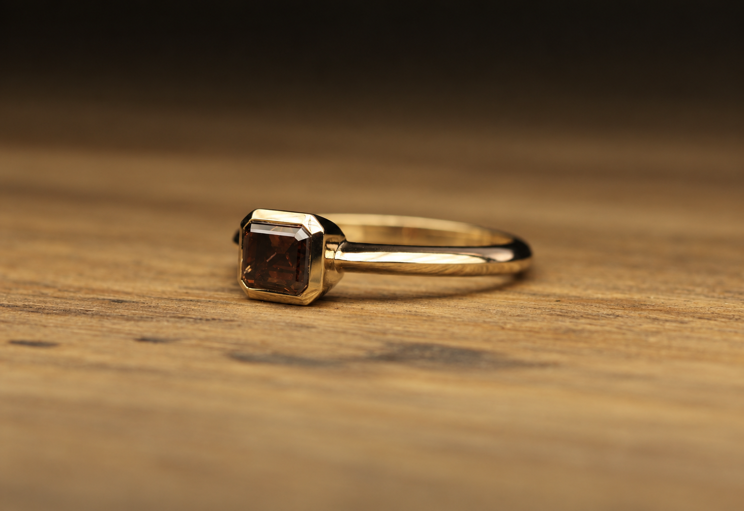 Gold ring with a square, dark brown gemstone on a wooden surface.