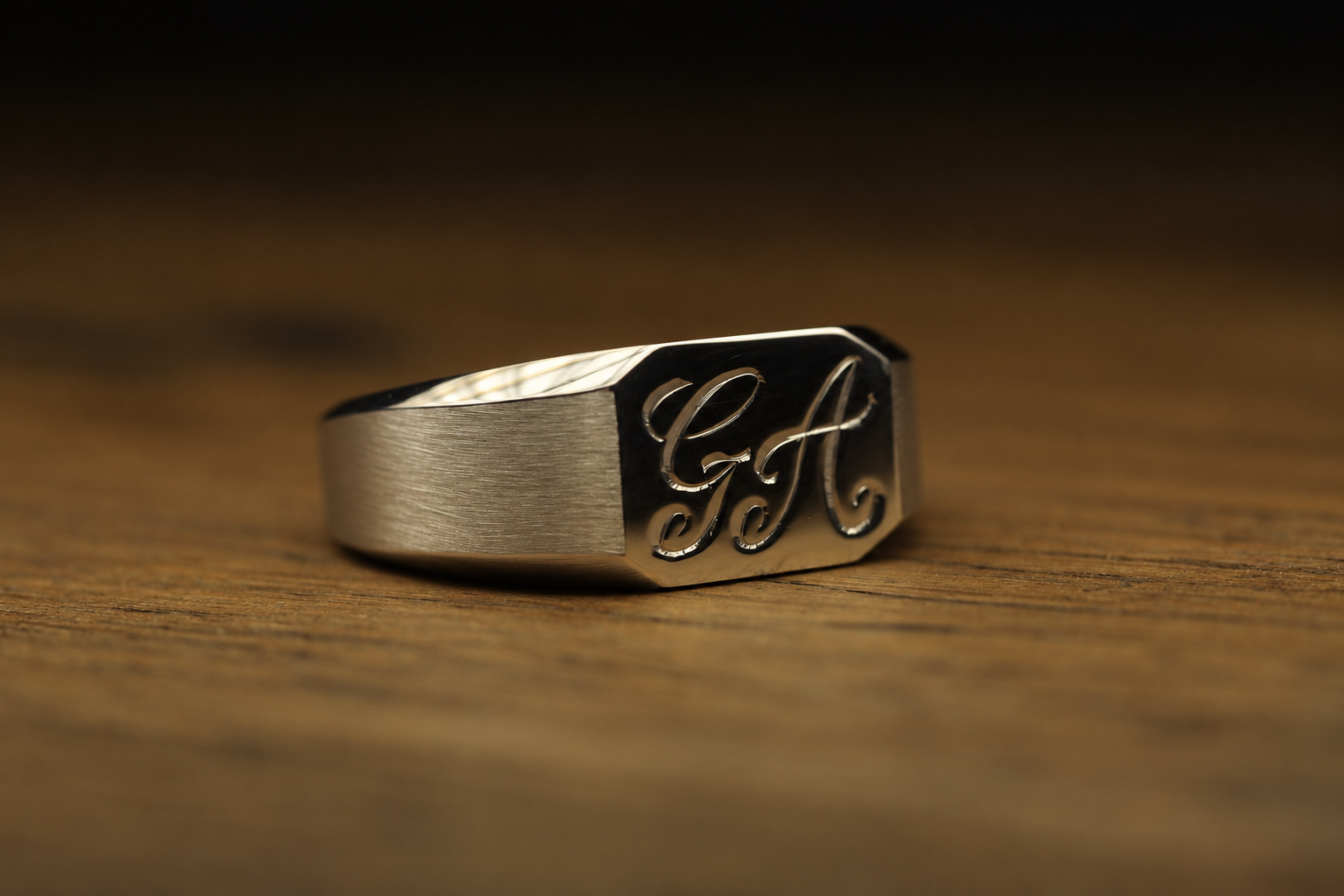 A stainless steel ring with engraved cursive initials 'G F' resting on a wooden surface.