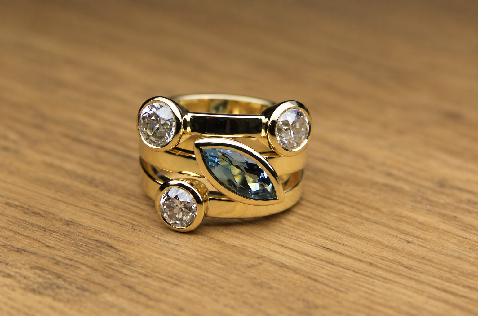 Gold jewelry rings with large clear stones, and one with a marquise-shaped blue-green stone, placed on a wooden surface.