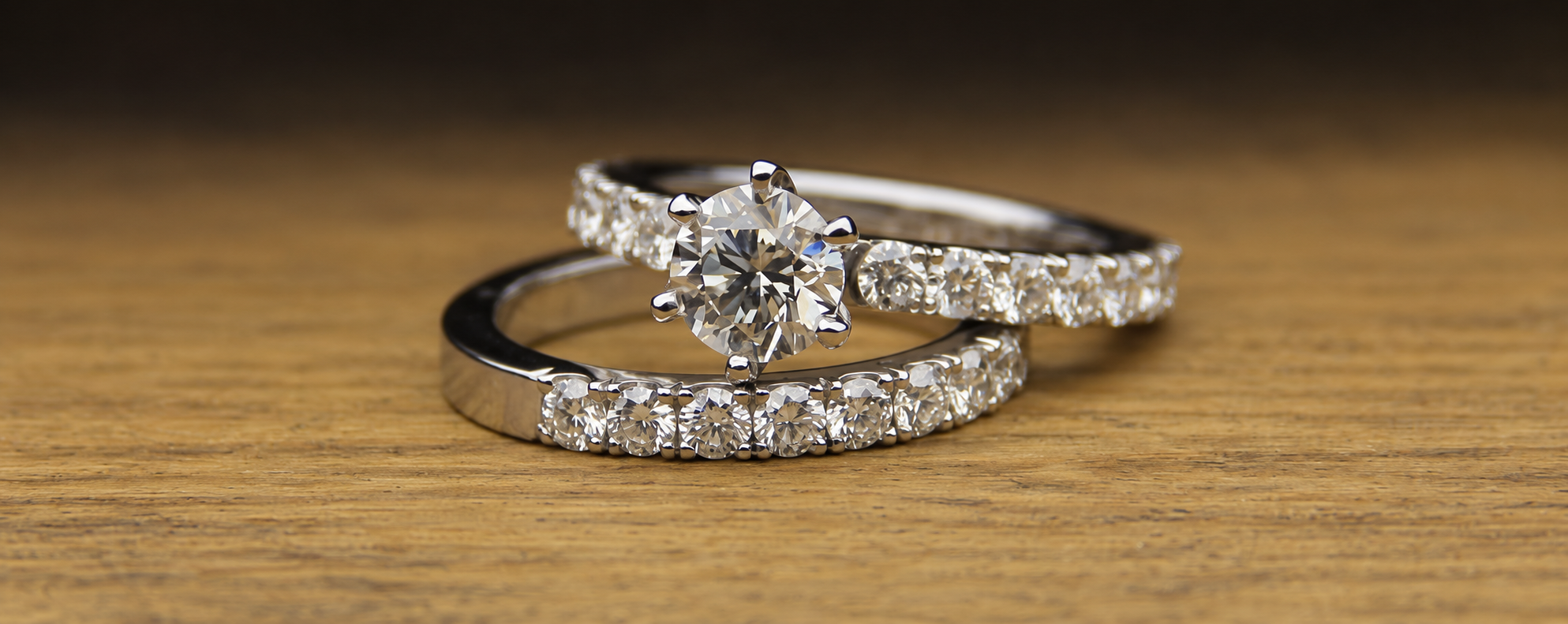 Three diamond engagement rings stacked on a wooden surface, featuring central round-cut diamonds and pavé-set diamonds on the bands.