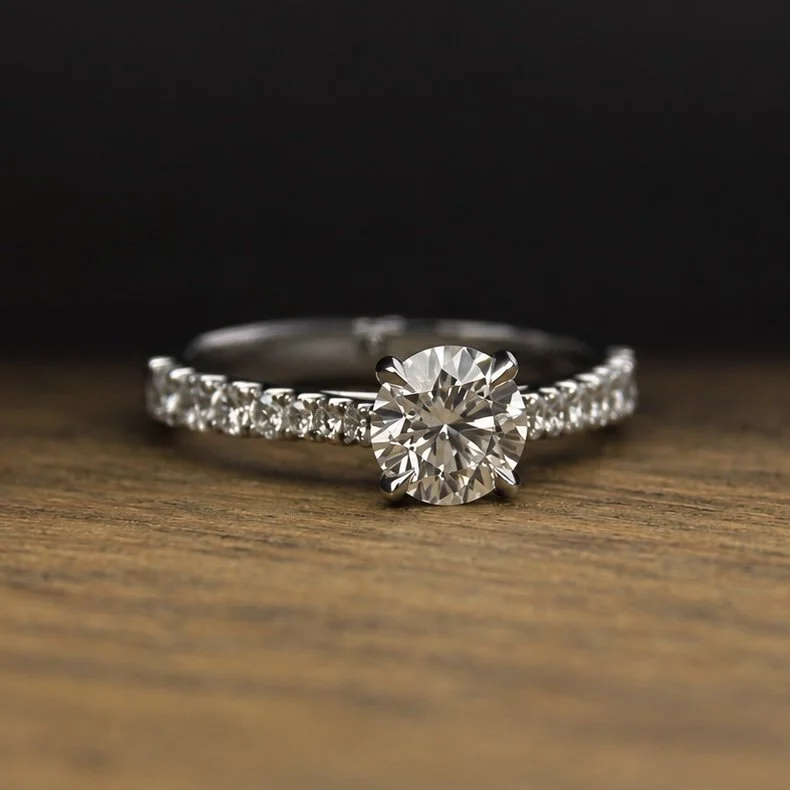 A sparkling diamond engagement ring with a large round center stone and a band encrusted with smaller diamonds, resting on a wooden surface.