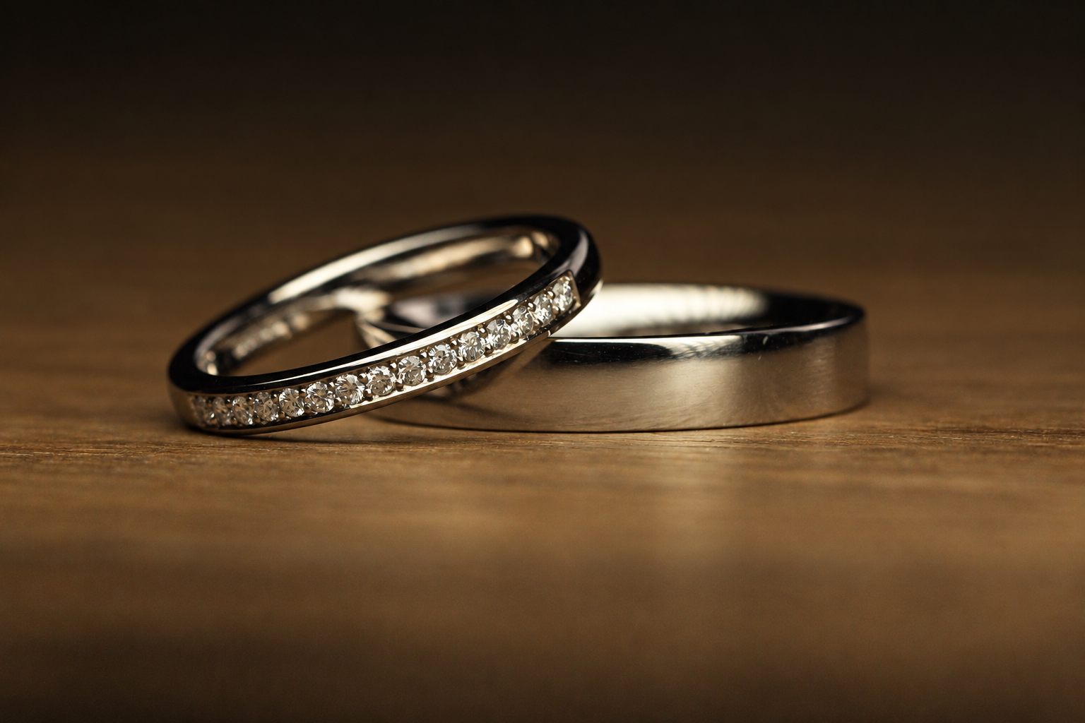 Three wedding rings placed on a wooden surface, one with small diamonds, one plain with a matte finish, and one plain with a shiny finish.