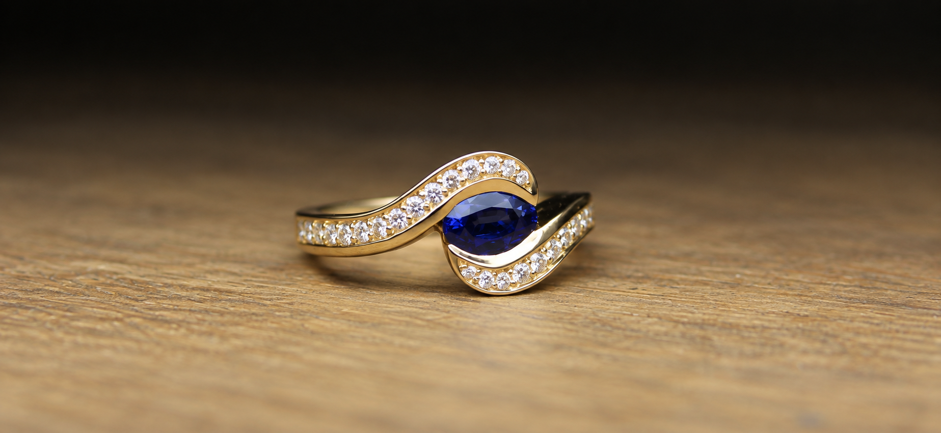 Gold ring with a large blue gemstone and small white diamonds on a wooden surface.