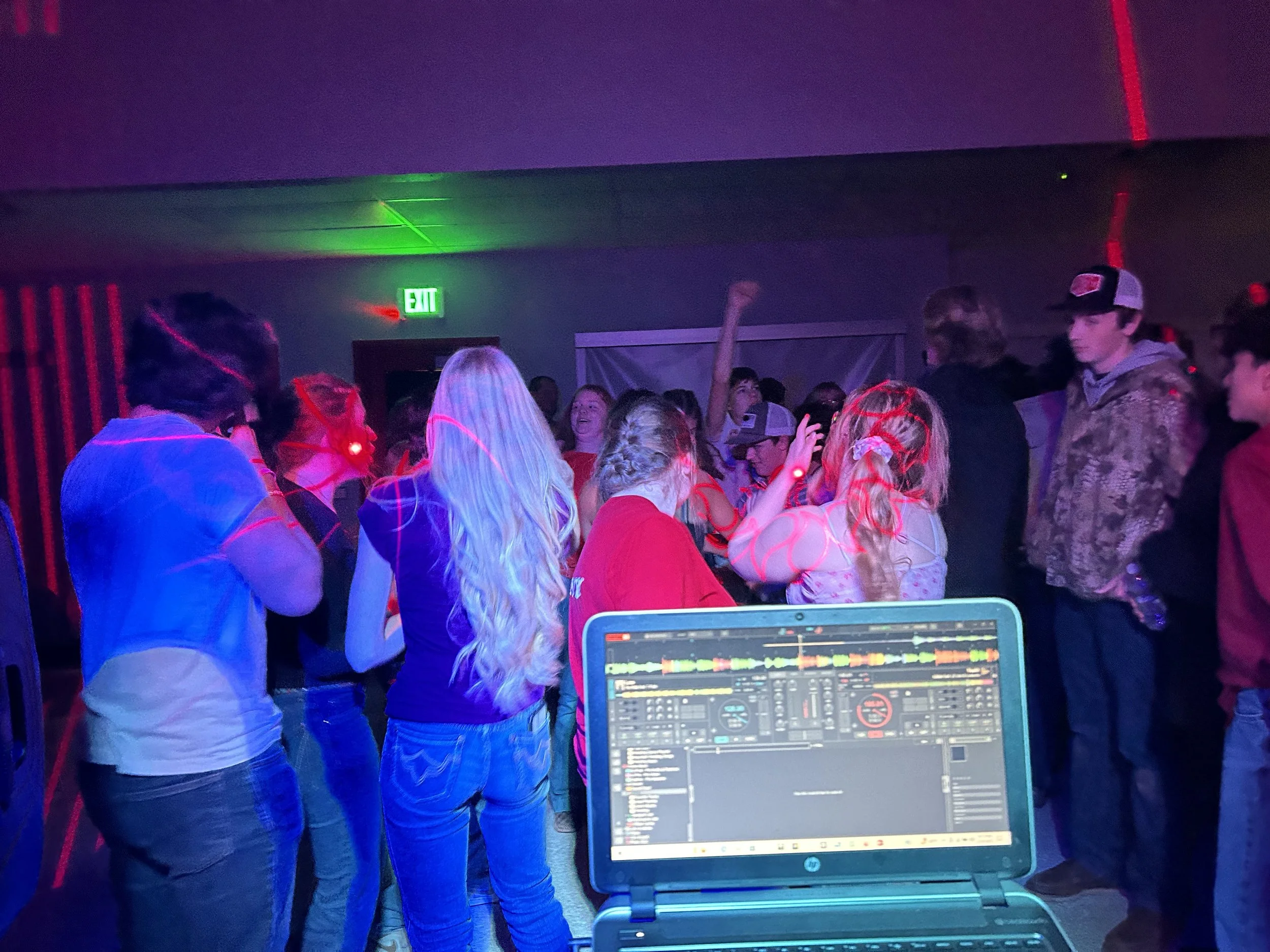 People dancing at a party with DJ equipment visible in the foreground.