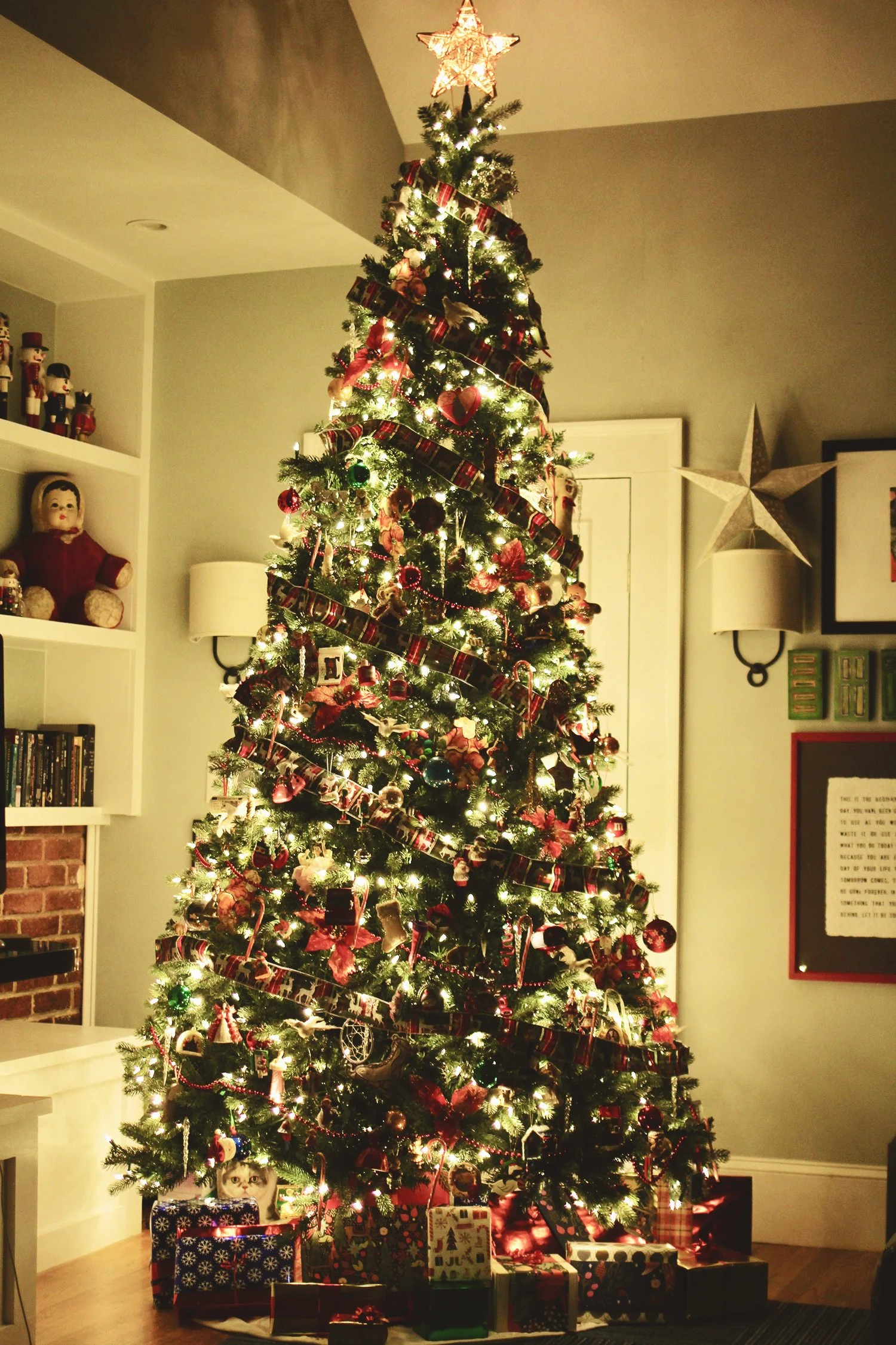 Christmas tree decorated with lights and ornaments, topped with a star, with wrapped presents at the base.