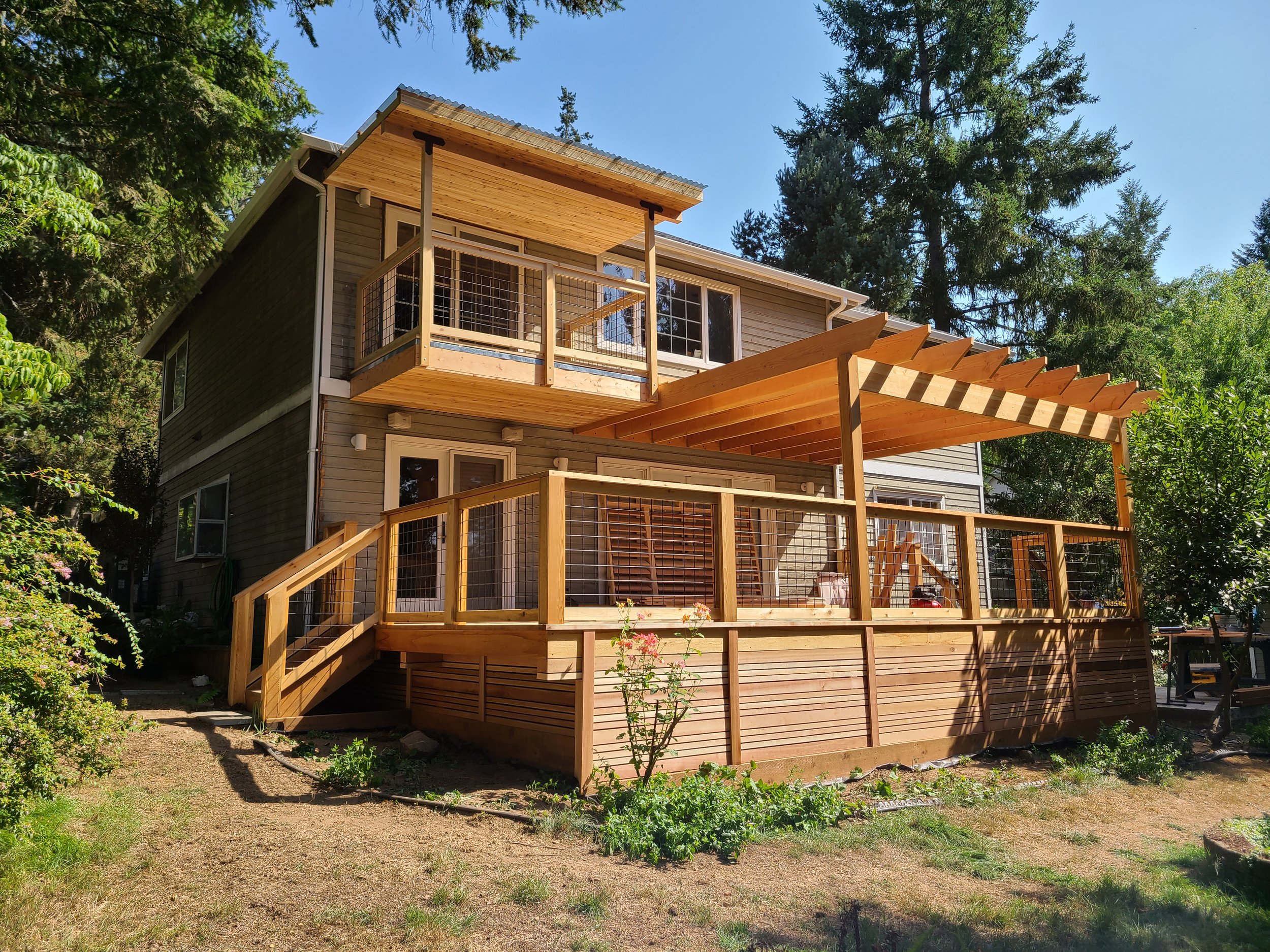 Two story house with large deck and pergola with a small balcony on second story