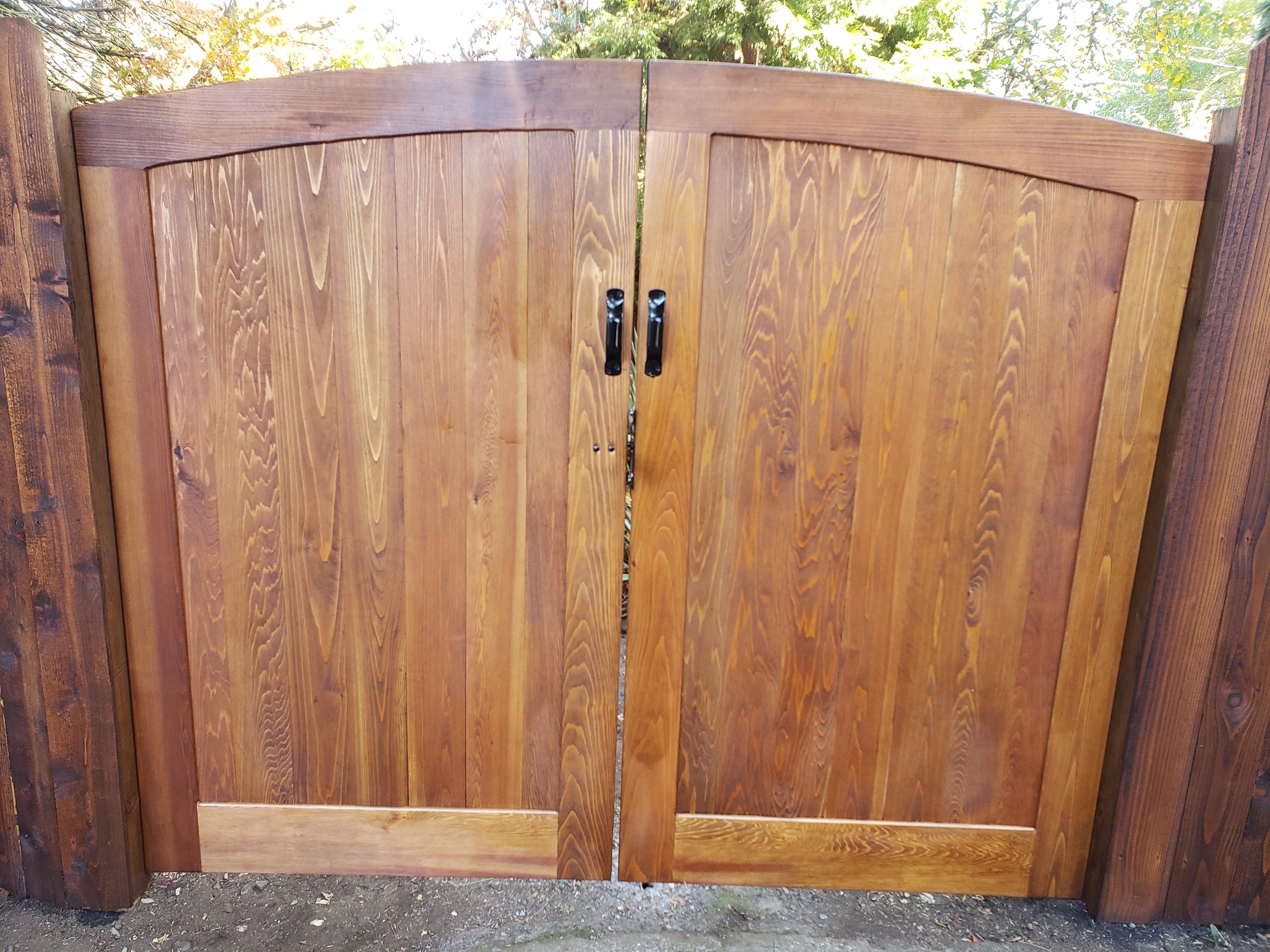 Wooden outdoor gate with vertical planks and black latch handles.