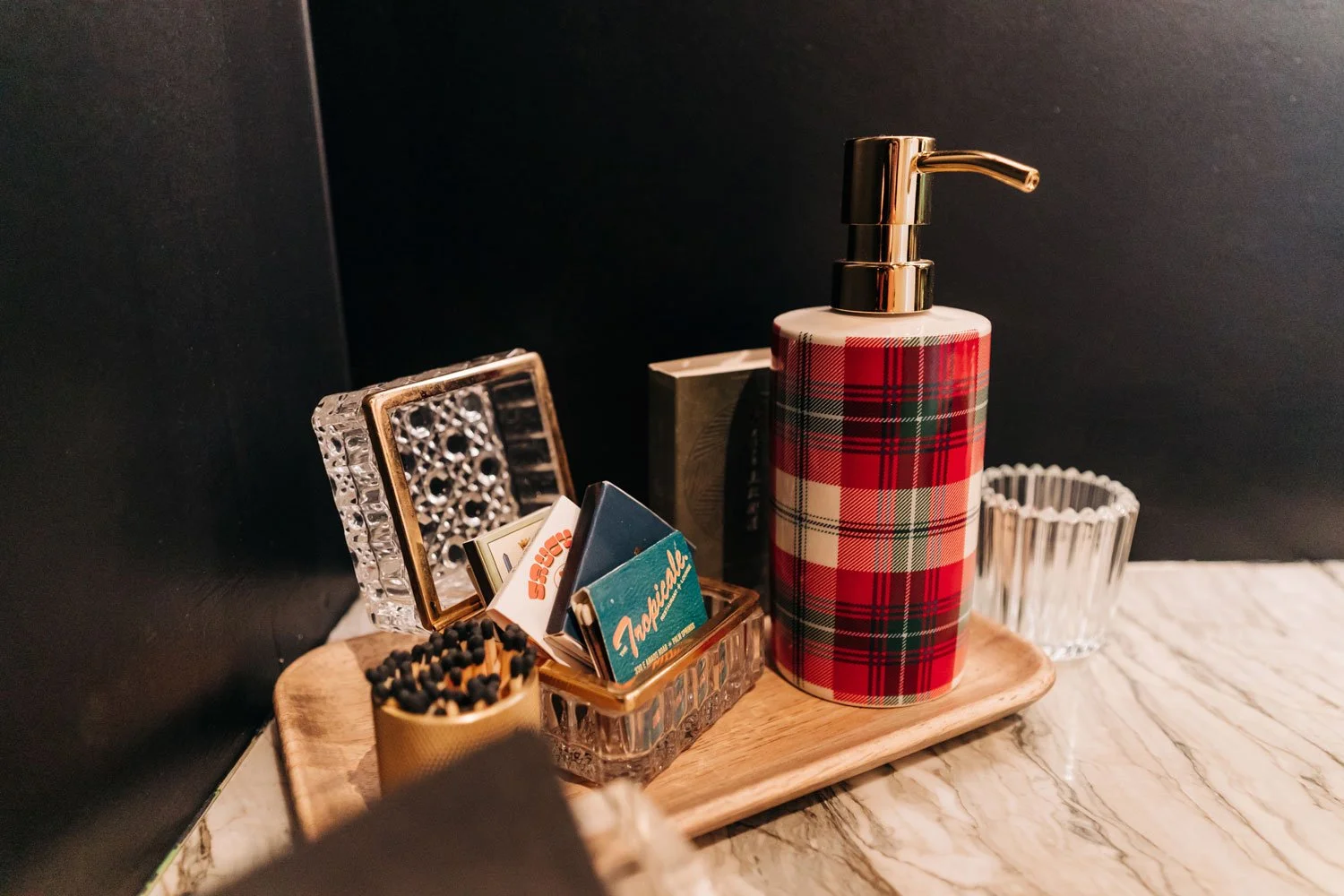 Holiday powder room styling: tartan plaid soap dispenser and matches on a marble counter against a black wall