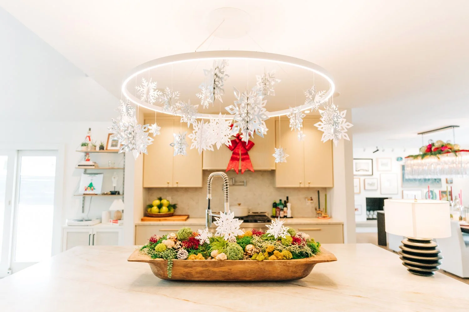 Kitchen island with a ring chandelier, hanging paper snowflakes, and a moss-and-pinecone holiday centerpiece