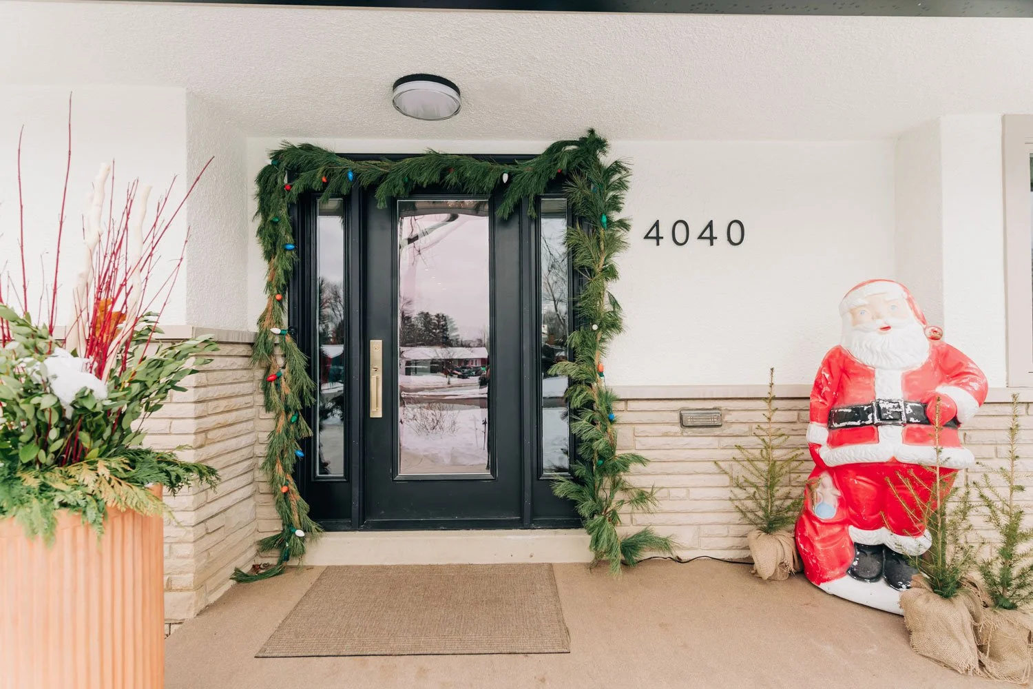 Black front door framed with fresh garland and vintage colored bulbs, vintage Santa blow mold beside it, Columbus holiday curb appeal