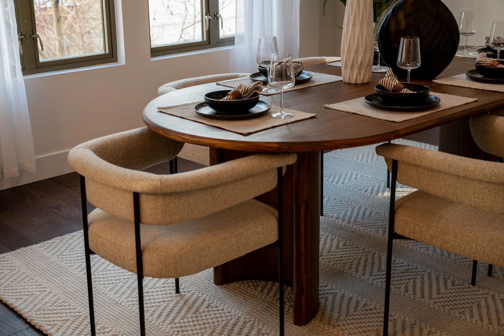 Modern dining room with wooden table, beige chairs, table setting, and large windows.