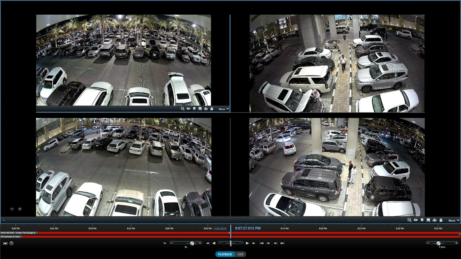 Surveillance footage showing various angles of a parking lot filled with cars at night. The scene includes parked cars, some people walking, and tall palm trees illuminated by streetlights.
