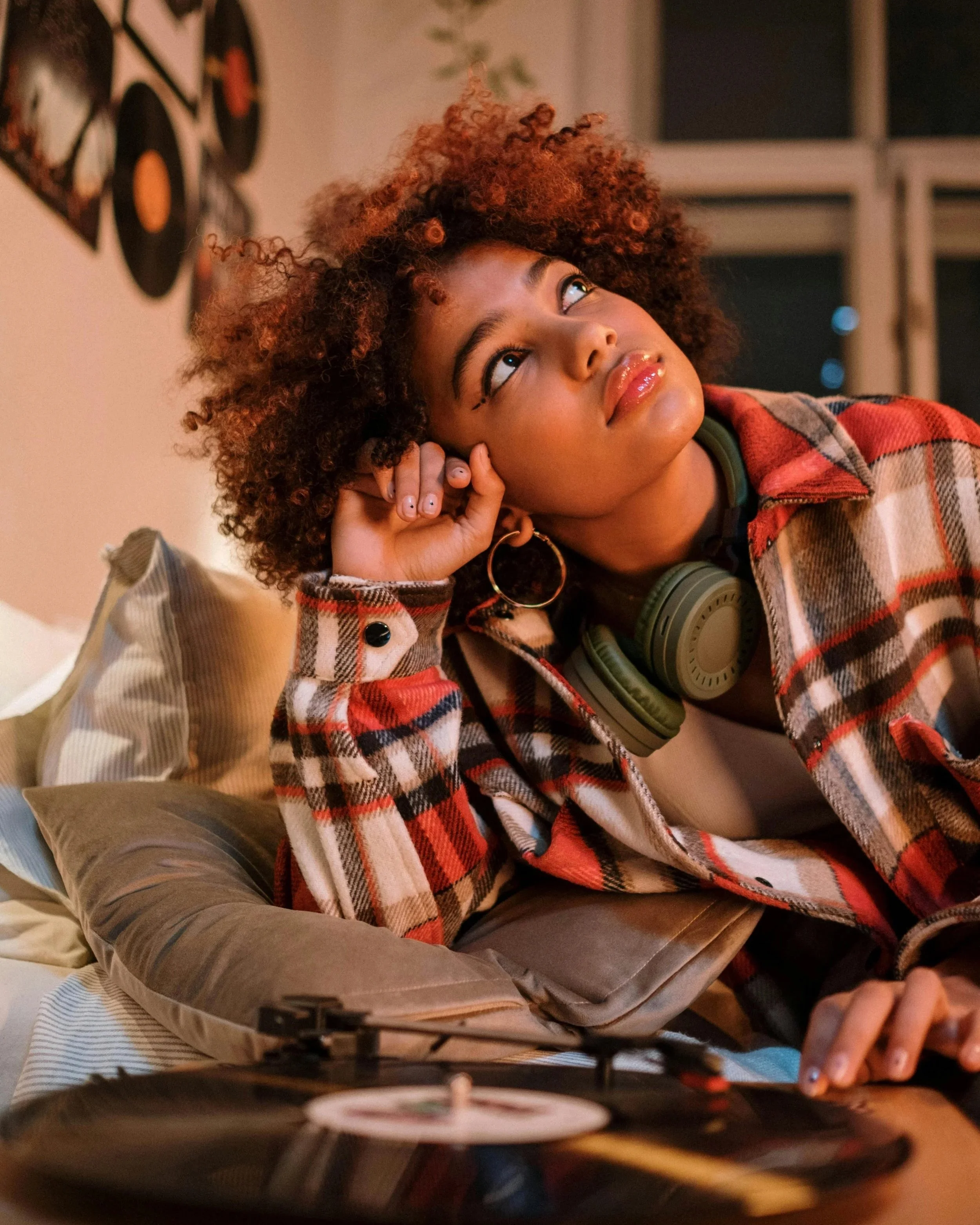 Black woman resting in a cozy room with headphones and vinyl records, reflecting softly during the winter season.