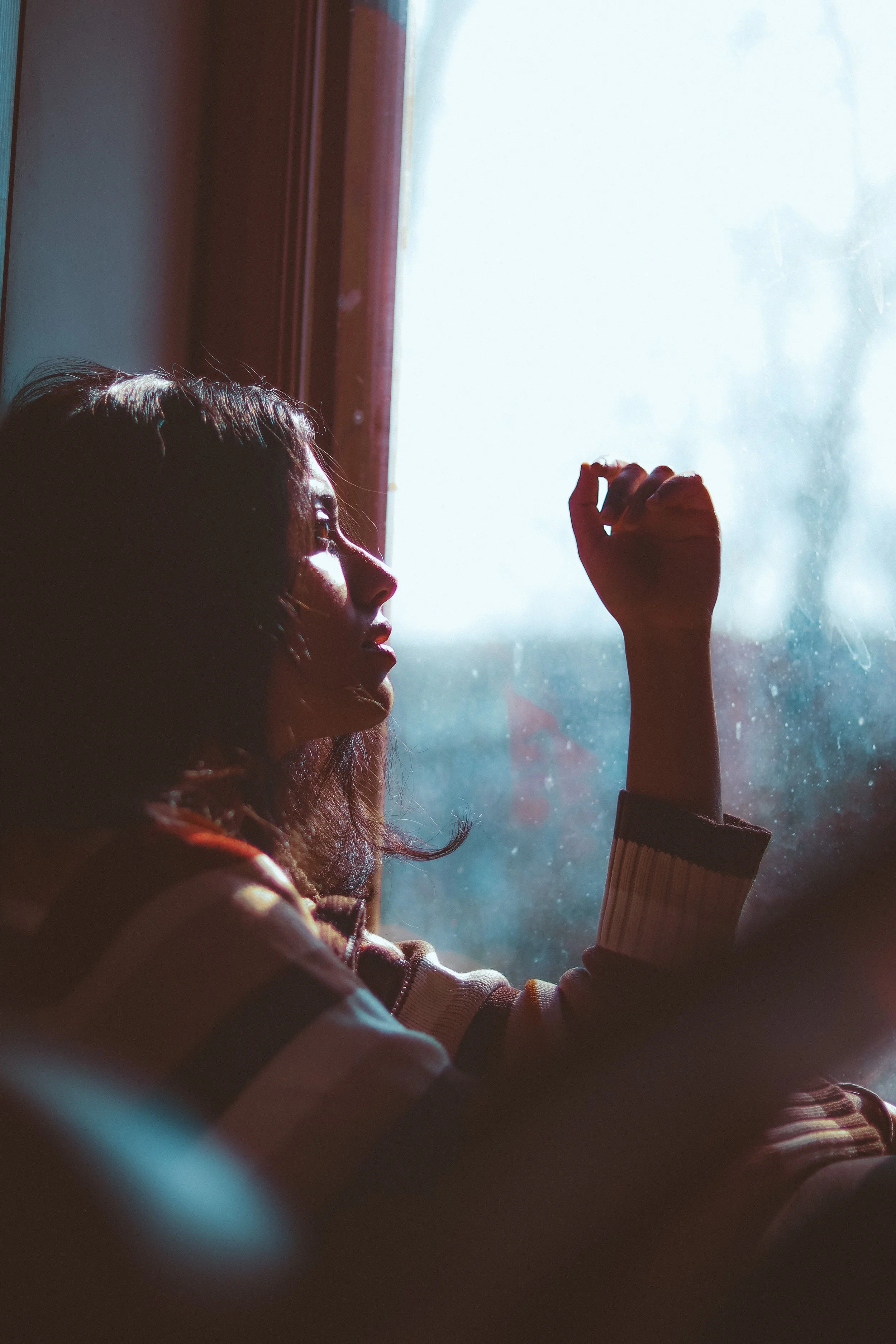 Woman sitting quietly by a window in deep reflection, representing reconnecting with herself after years of living in survival mode.