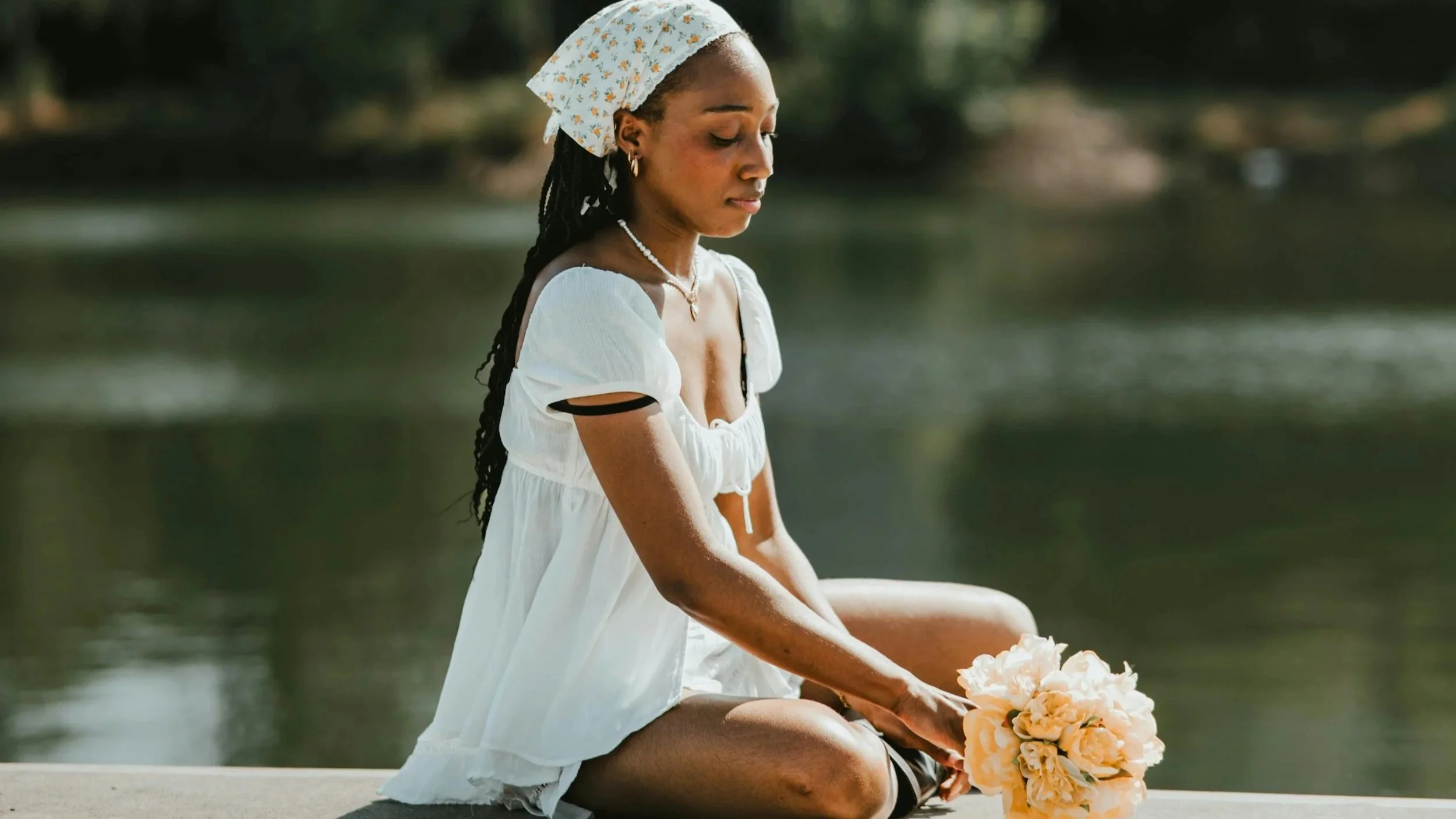 Black woman sitting by water holding bouquet, peaceful and reflective — self-care therapy Bowie MD.