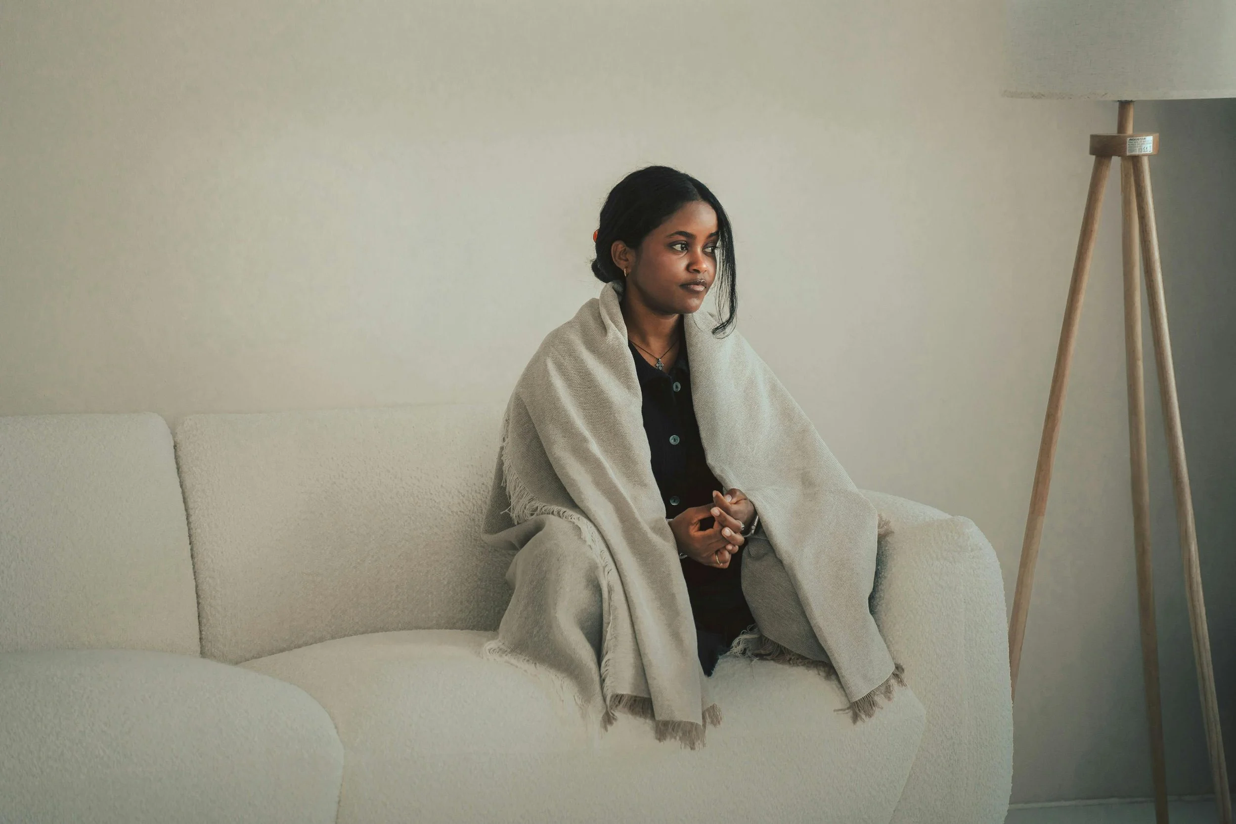 Woman sitting quietly on a sofa wrapped in a blanket, reflecting emotional overwhelm and the experience of carrying too much
