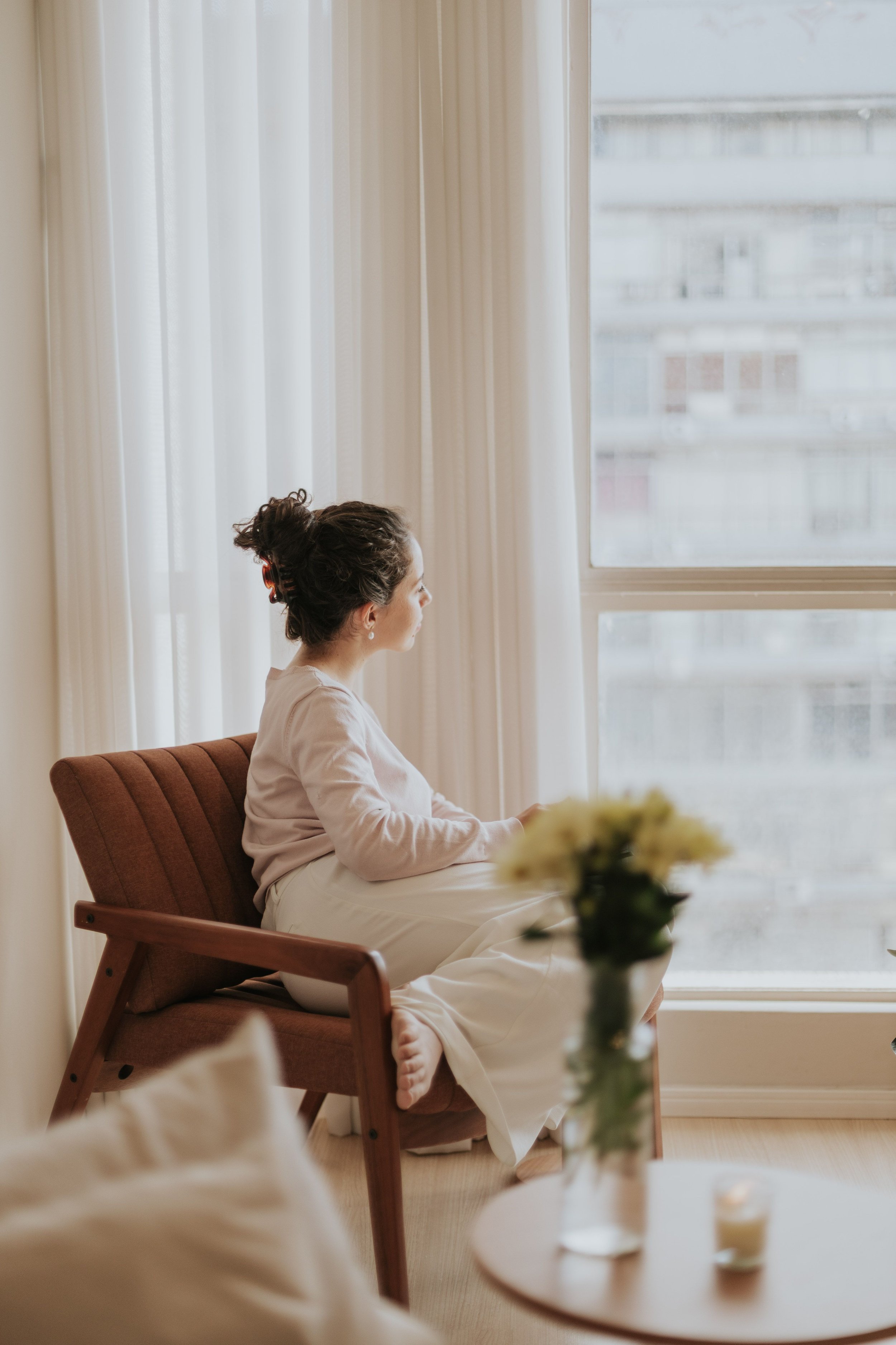 Woman in a reflective state, sitting in chair looking out of the window representing Online Brainspotting trauma therapy for high-achieving women