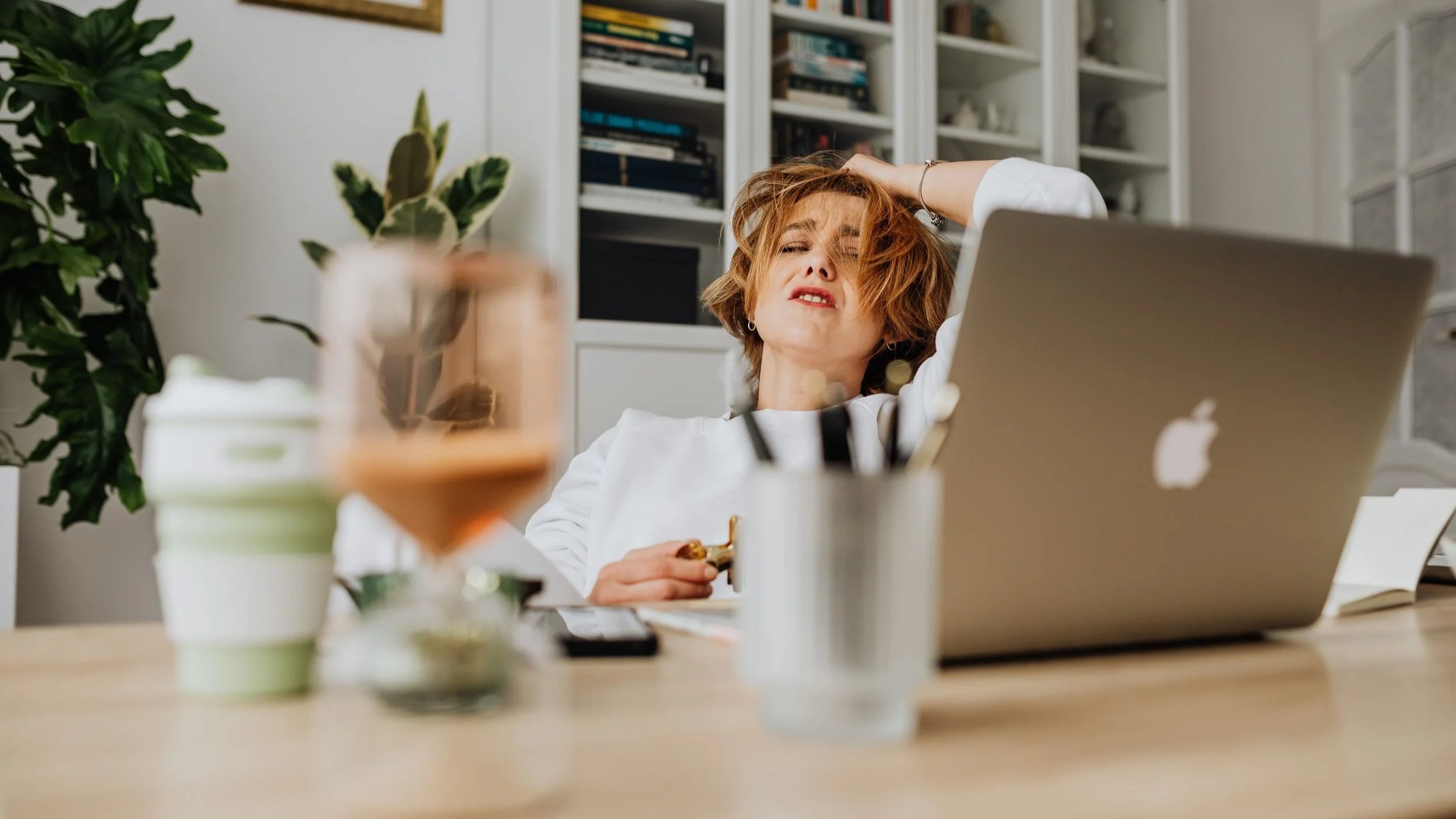 Woman working on a laptop and appearing overwhelmed at her desk, illustrating seasonal anxiety, stress, and mental overload.