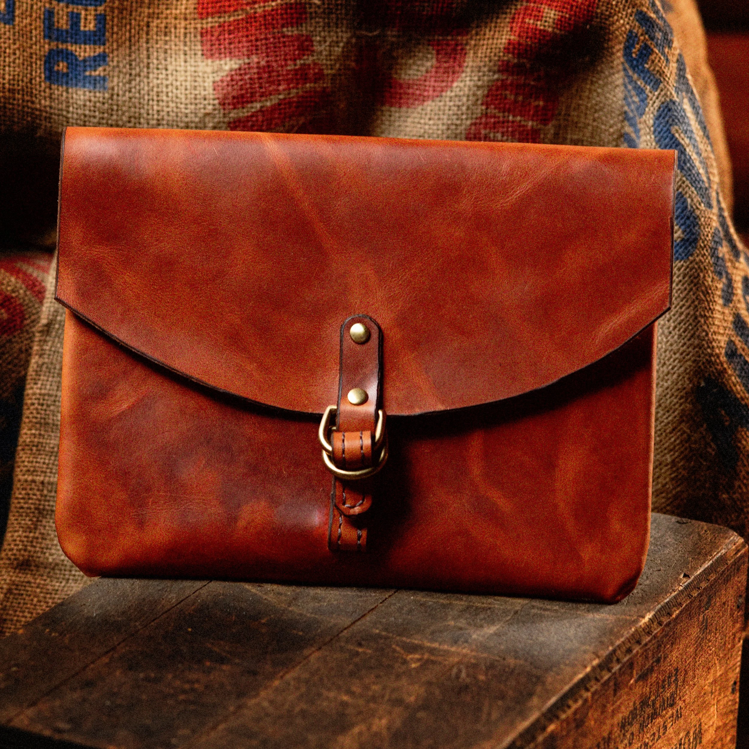 Brown leather clutch purse with a buckle closure placed on a wooden surface.