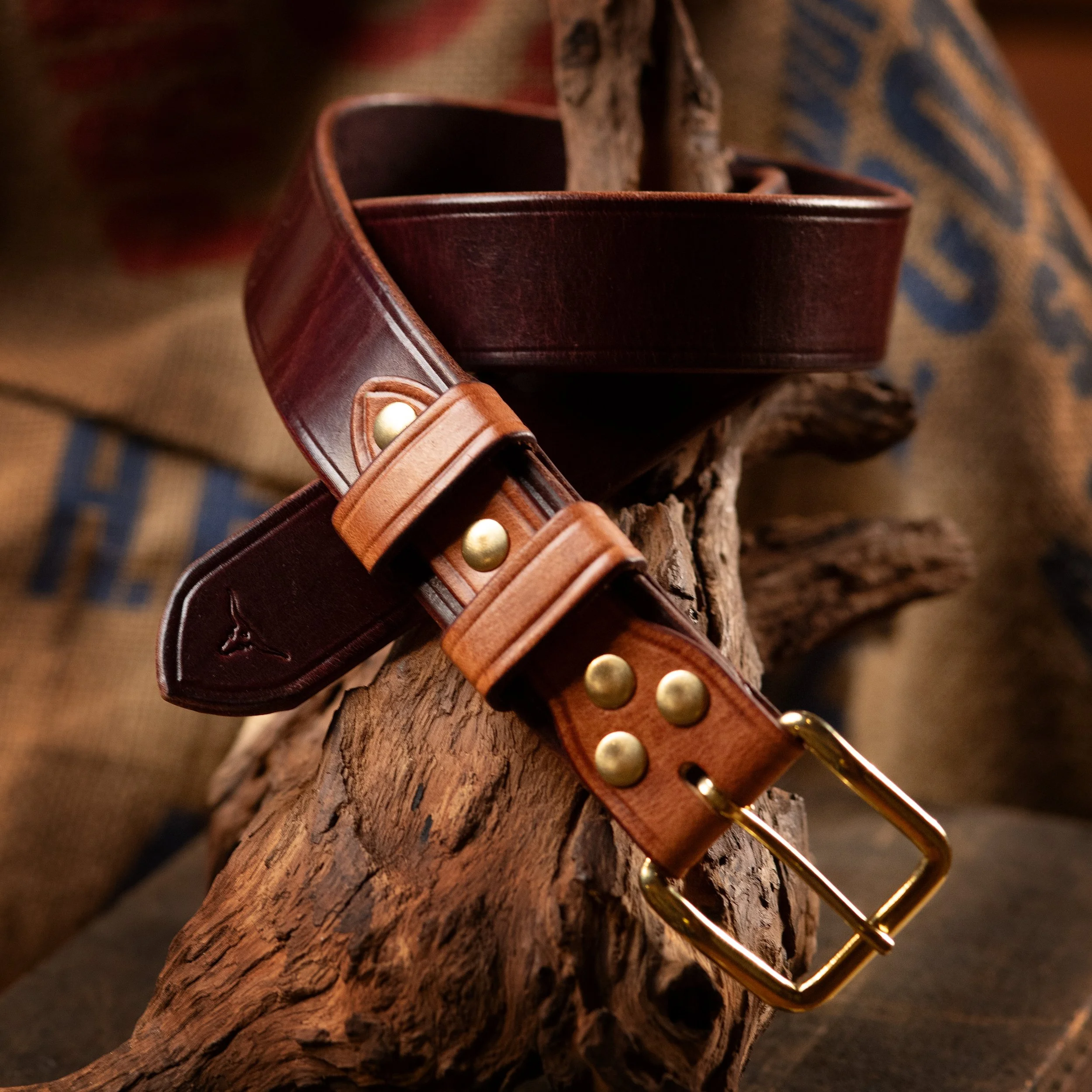 Close-up of a brown leather belt with brass hardware resting on a piece of wood with textured background.